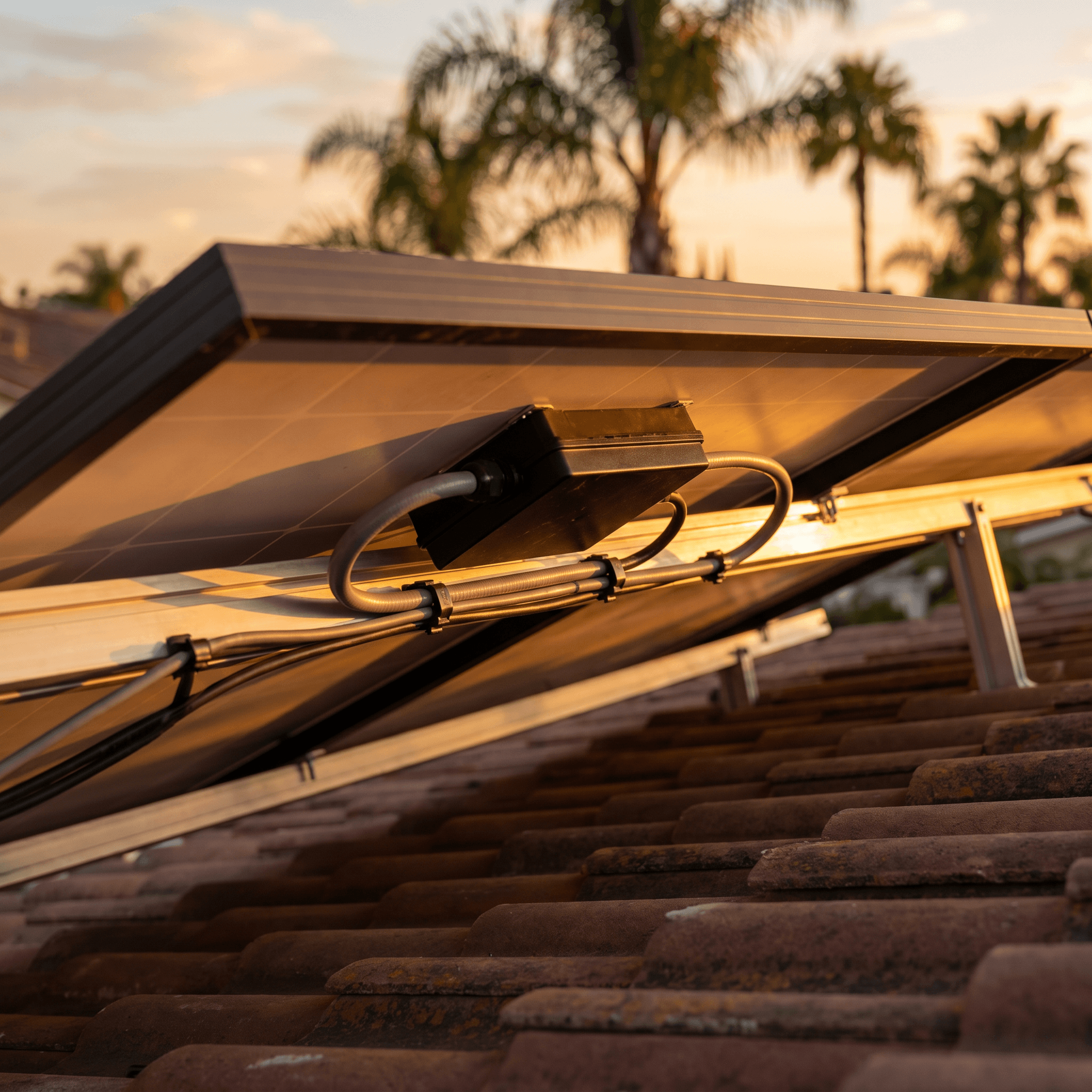 Close-up of a black microinverter mounted under a solar panel on a Southern California tile roof