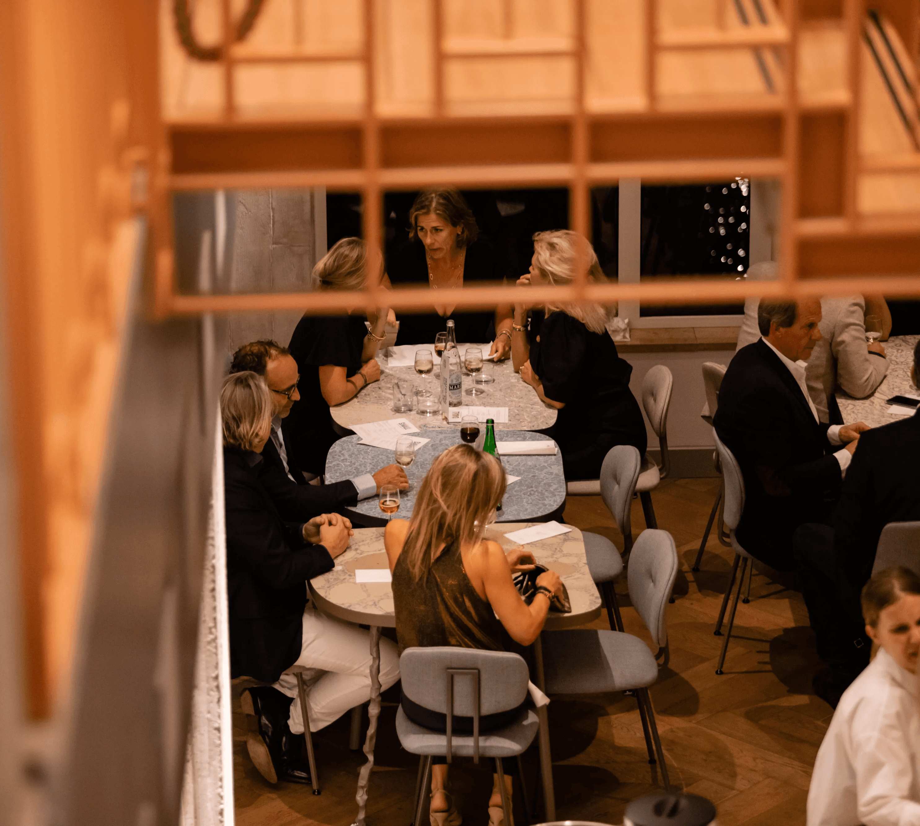 A cozy dining scene inside a wooden structure with guests enjoying a meal and soft lighting.