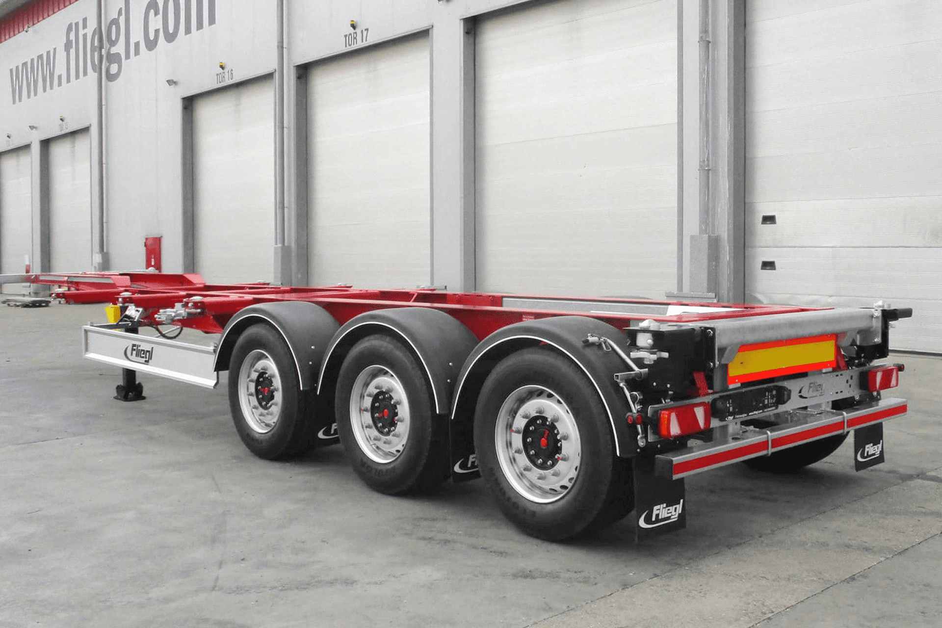 Red container chassis trailer with three axles parked outside a truck equipment facility