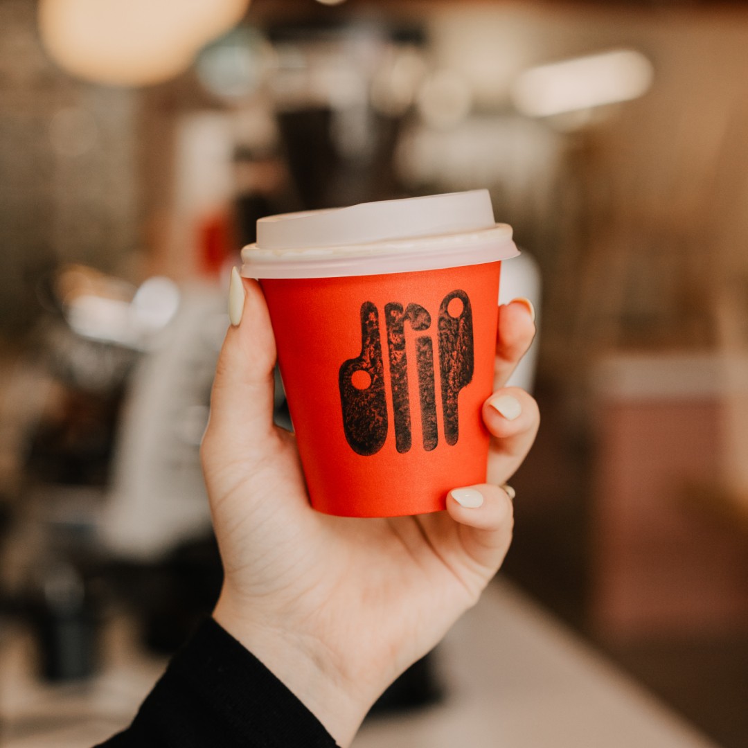 A hand holding an orange takeaway coffee cup