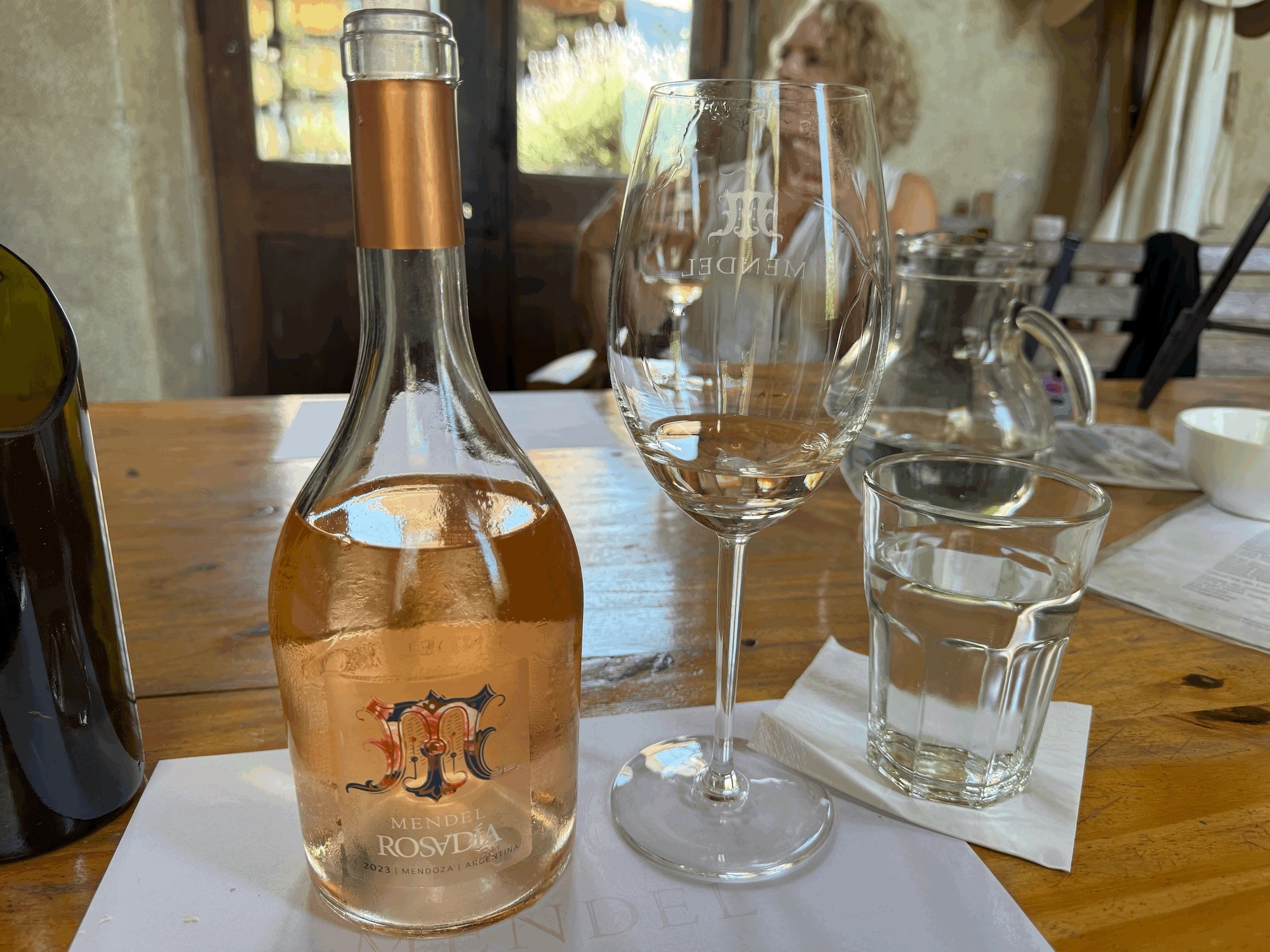 Bottle of 2023 Mendel Rosadía rose beside an engraved Mendel wine glass during a tasting in Mendoza