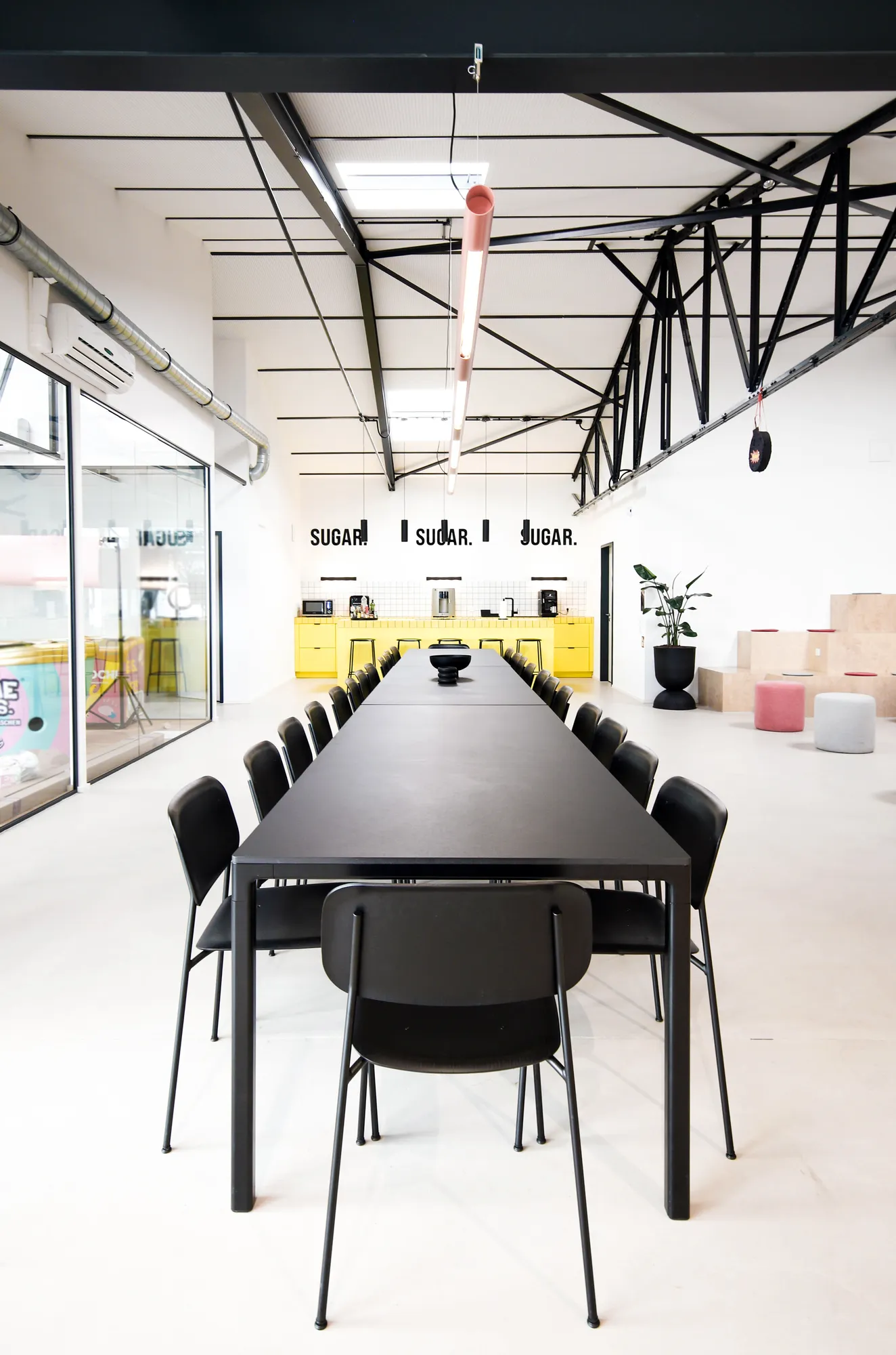 Long black dining table with chairs leading to the yellow SUGAR kitchen in the hall.
