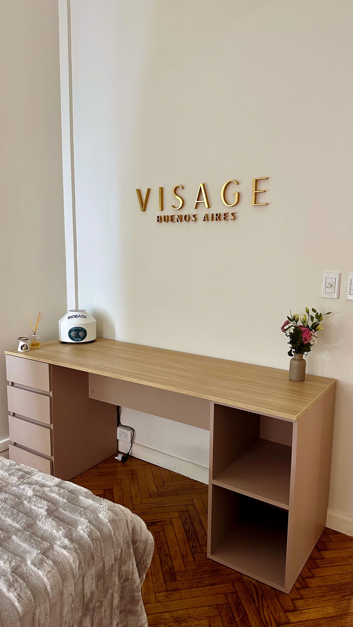 A serene and elegant spa space with wooden reclining chairs and white cushions. Golden sunlight filters through a cascading water feature, creating a peaceful atmosphere. Tropical plants and candles add to the relaxing ambiance.