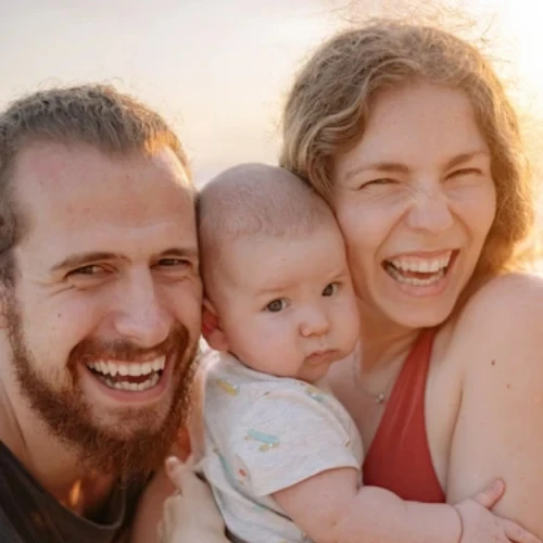Smiling parents holding their healthy infant outdoors, serving families across Melbourne's northern suburbs.