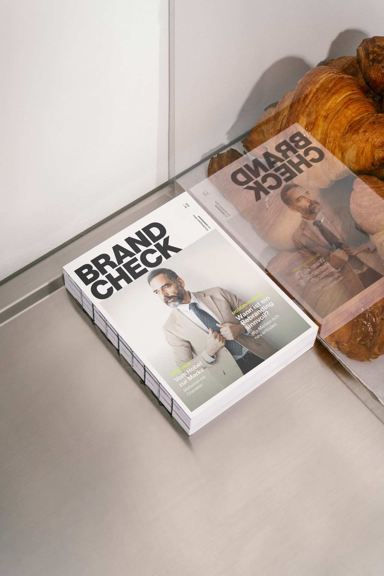 Close-up portrait of a person wearing a gray insulated hooded jacket with the hood up, showing their face framed by the hood against a light background.