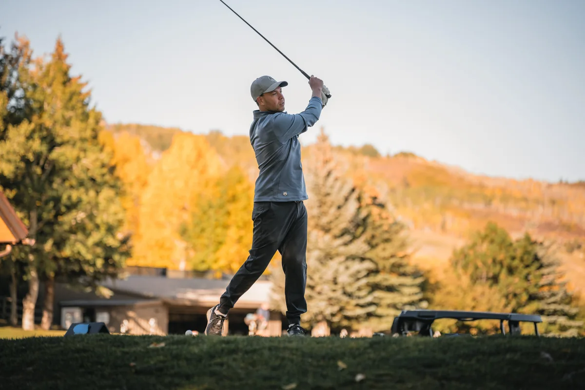 A retreat guest follows through on a golf swing beside golden autumn trees.