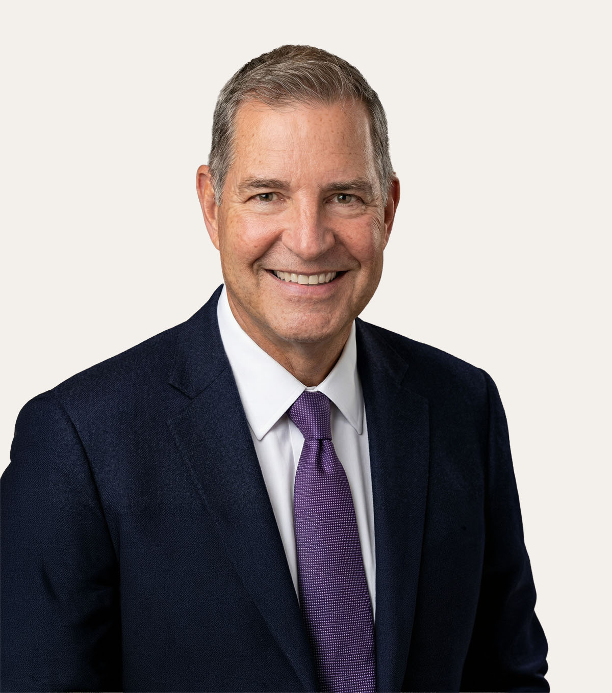 A man in a blue suit and purple tie smiles at the camera.