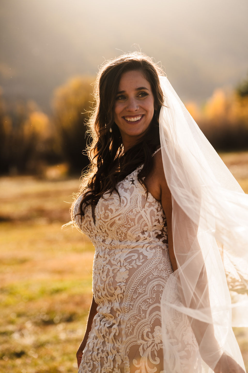 A joyful candid portrait of the bride smiling during golden hour, her lace wedding dress and sheer veil illuminated by the warm light of a Silverton afternoon.