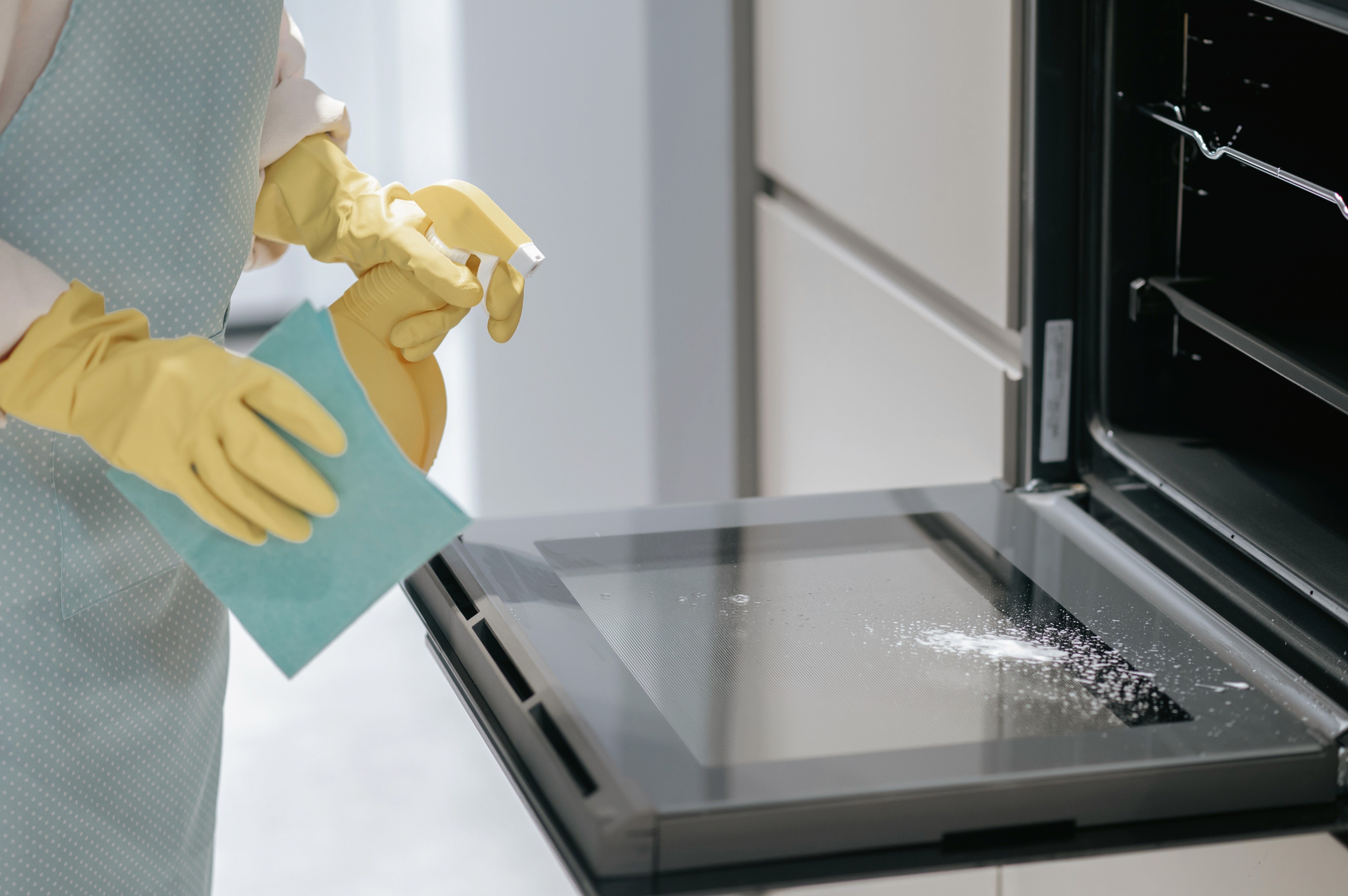 Professional cleaning oven with spray cleaner and microfiber cloth wearing yellow gloves
