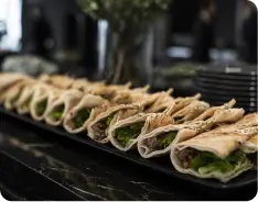 Mini wraps gourmet alinhados sobre bancada escura em serviço de catering premium, preparados para recepção corporativa elegante.