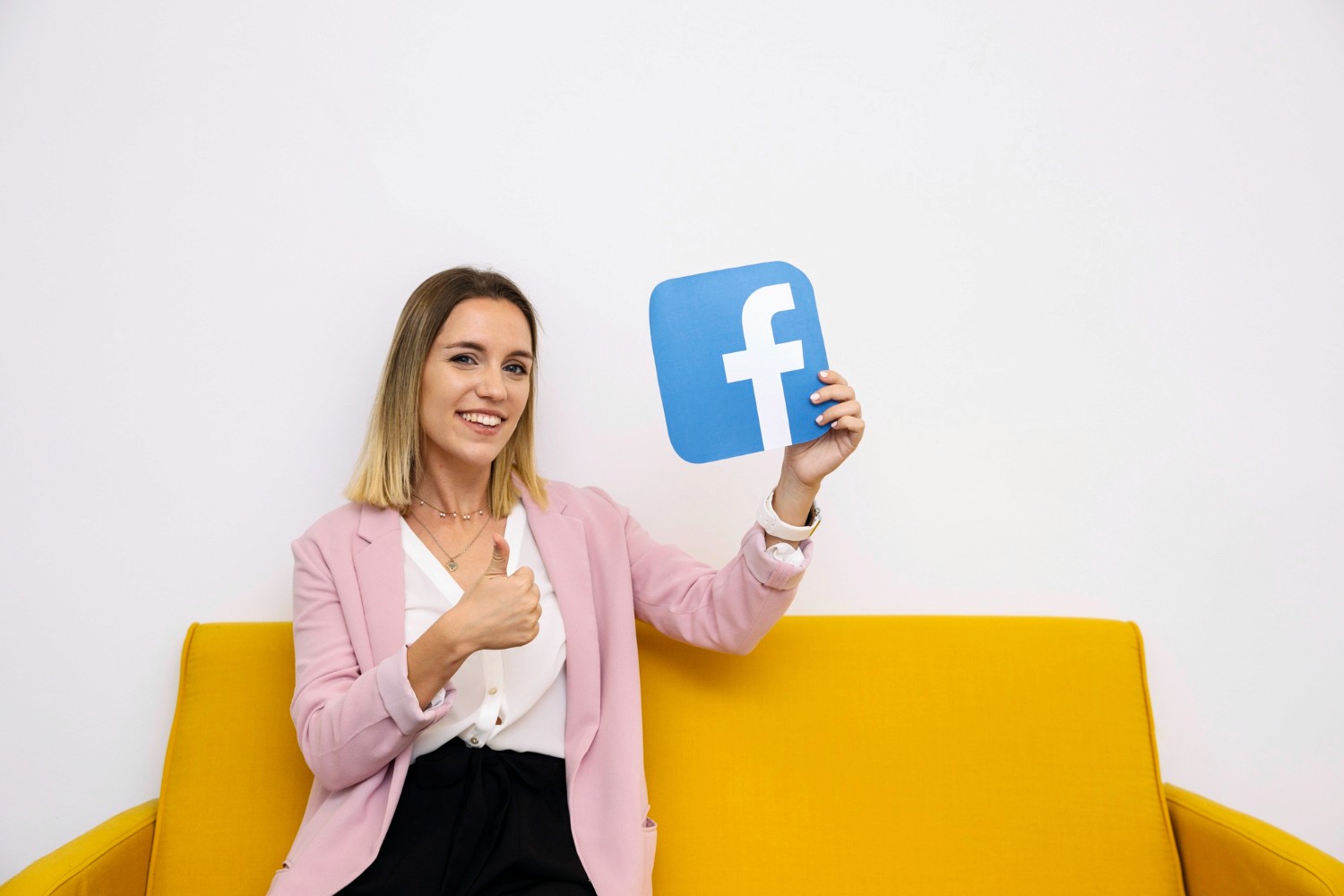  A woman seated on a couch, proudly displaying a Facebook sign with a smile on her face.