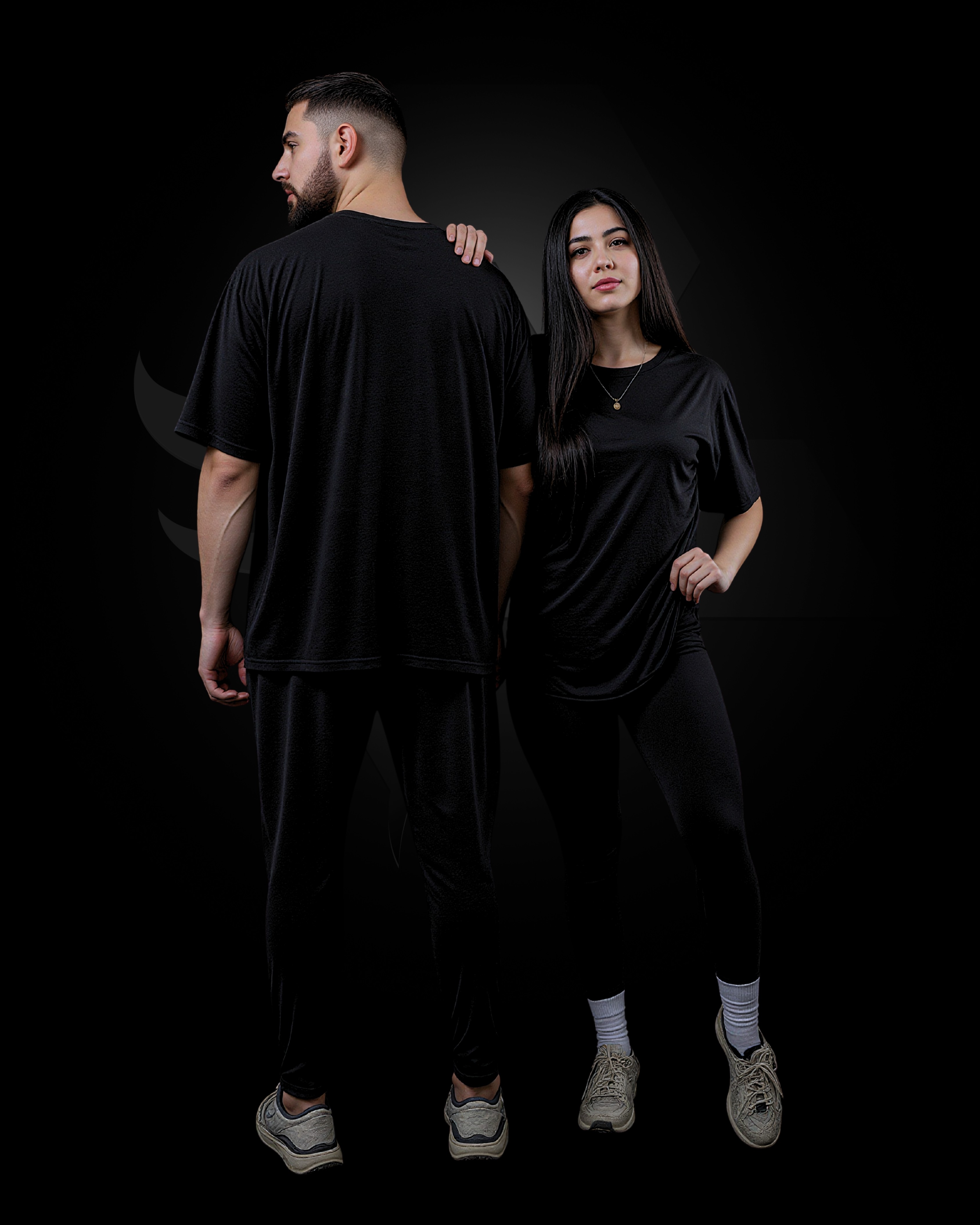 Man and woman in matching black outfits posing. The man is wearing a t-shirt and sweats, and the woman is wearing a black t-shirt and leggings.