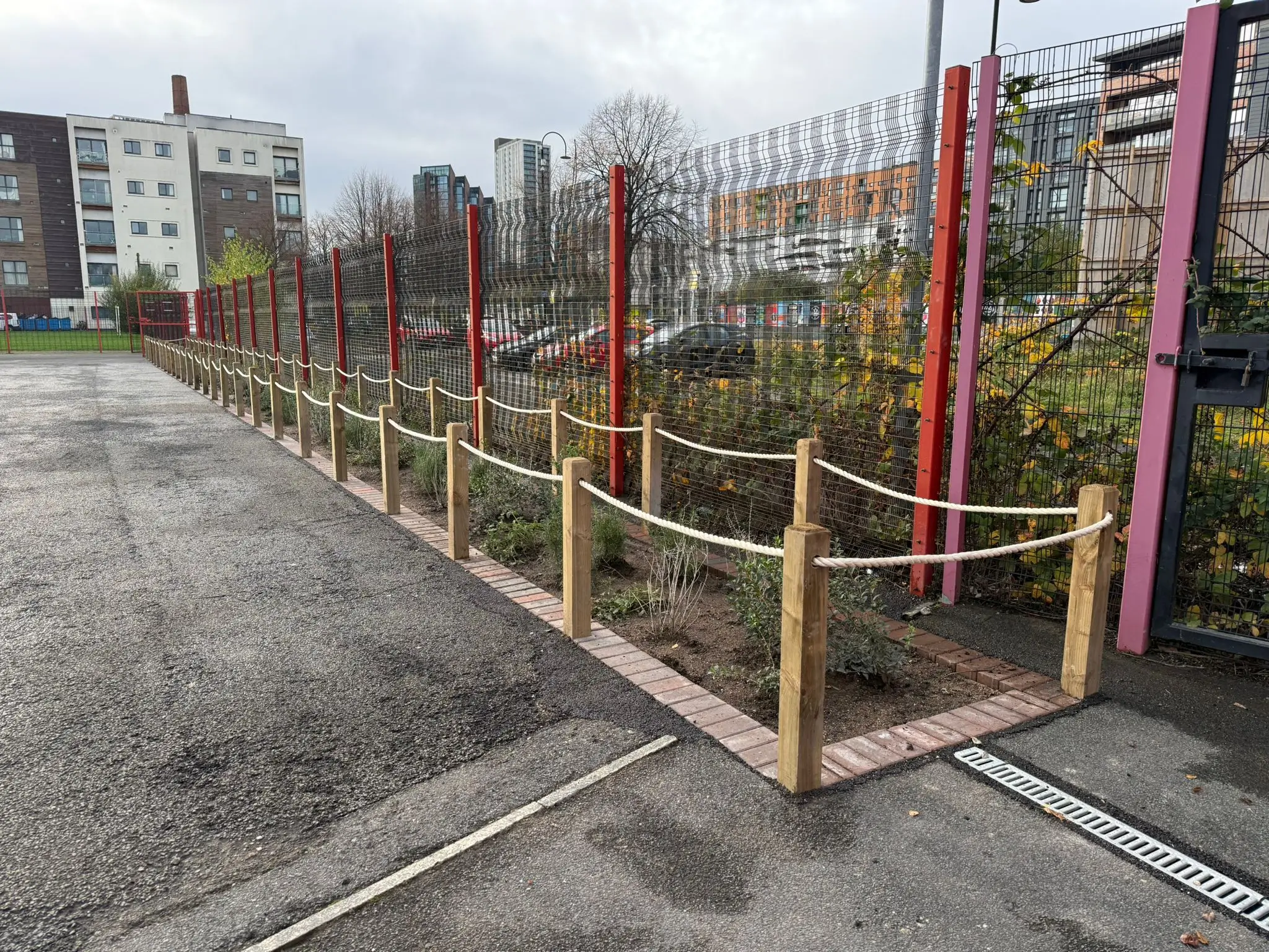 A vacant outdoor space with wooden and red barriers, surrounded by greenery and buildings in the background.