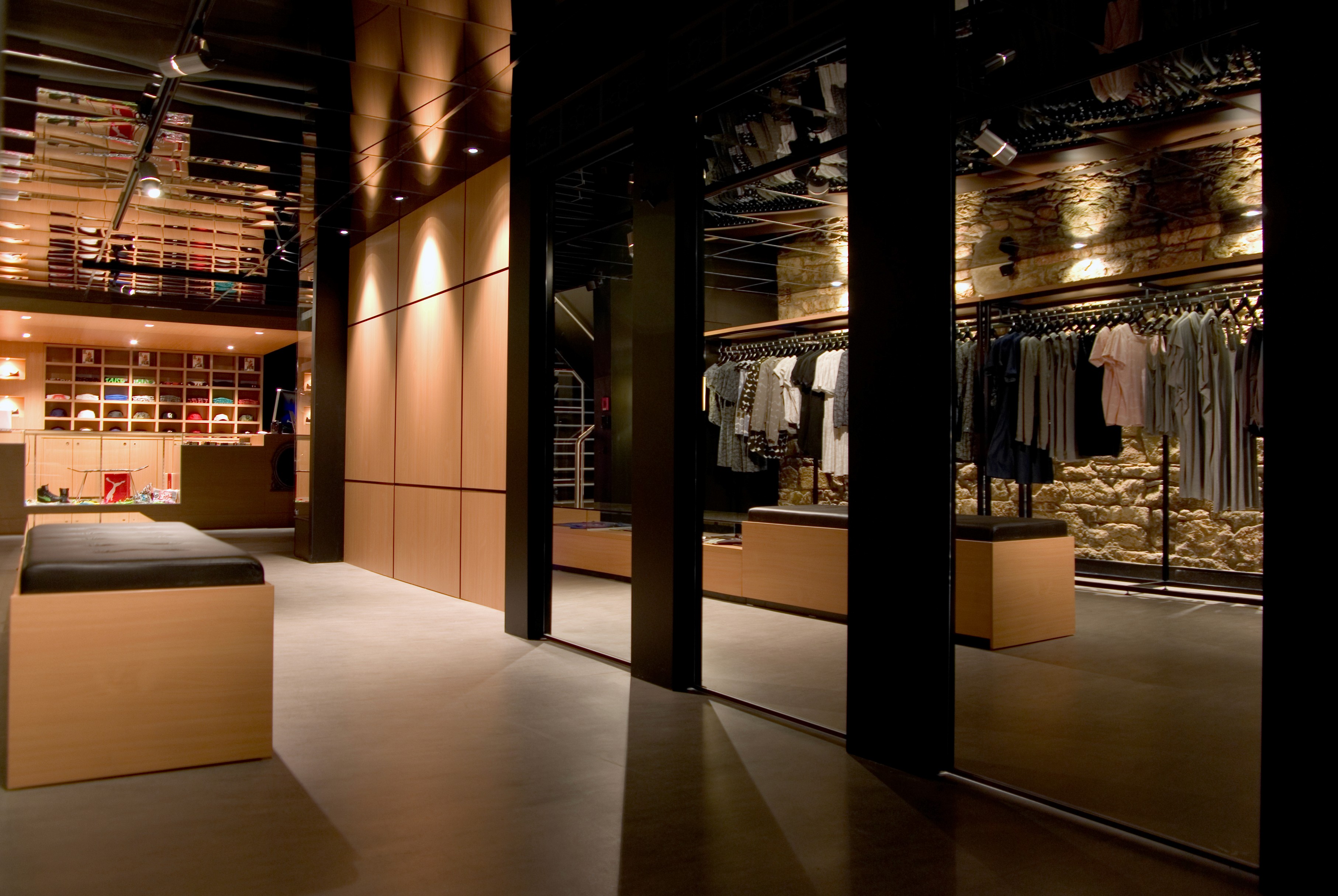 Main retail floor at Apartment Store featuring timber joinery, mirrored columns, and exposed stone wall with hanging apparel.