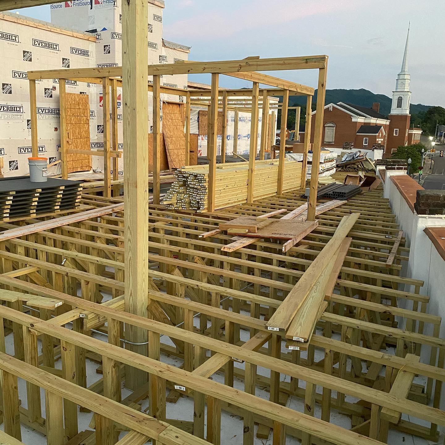 Construction site with wooden framework and beams against a backdrop of buildings and sky.