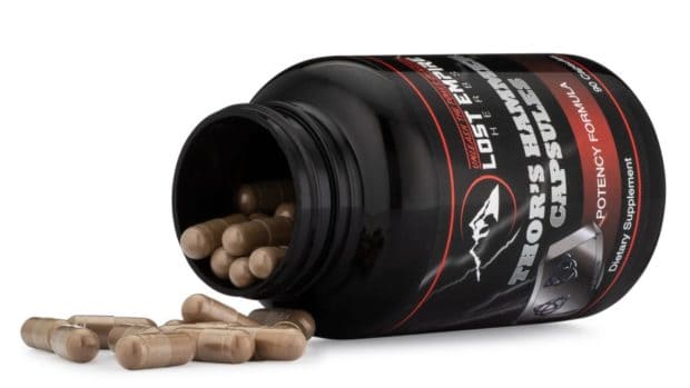 A black bottle of dietary supplement capsules is tipped over, with several capsules spilling out. The label features bold text and graphics.