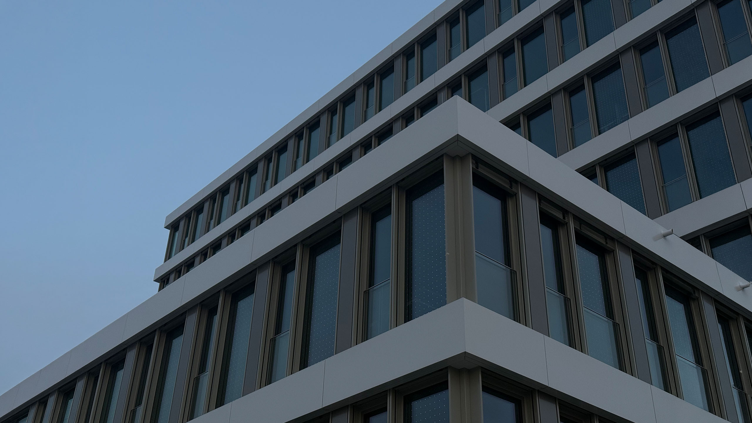 Moderne Bürogebäudefassade mit Glas- und Metallelementen vor blauem Himmel
