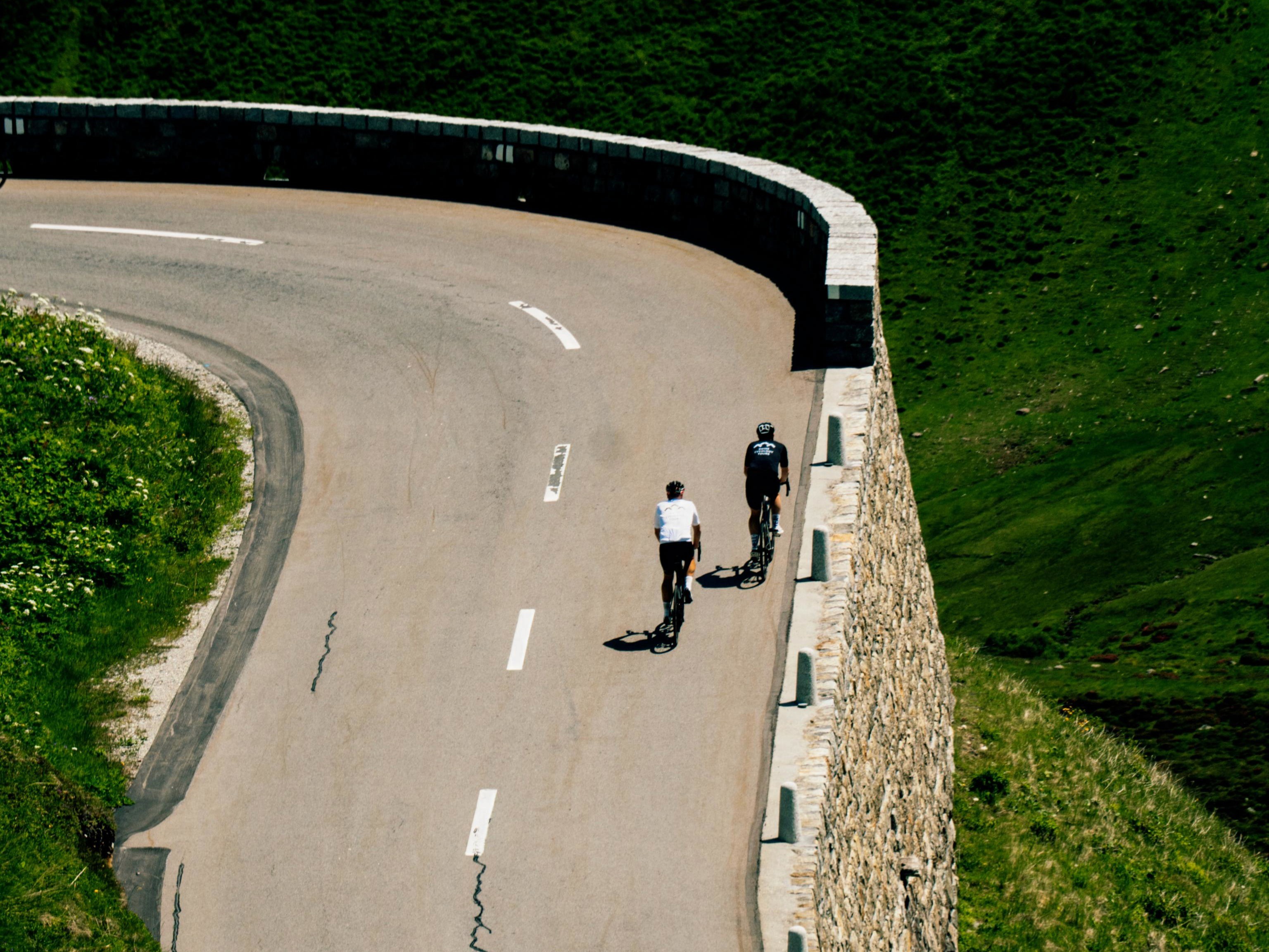Two lone cyclists riding up a mountain pass in the Swiss Alps
