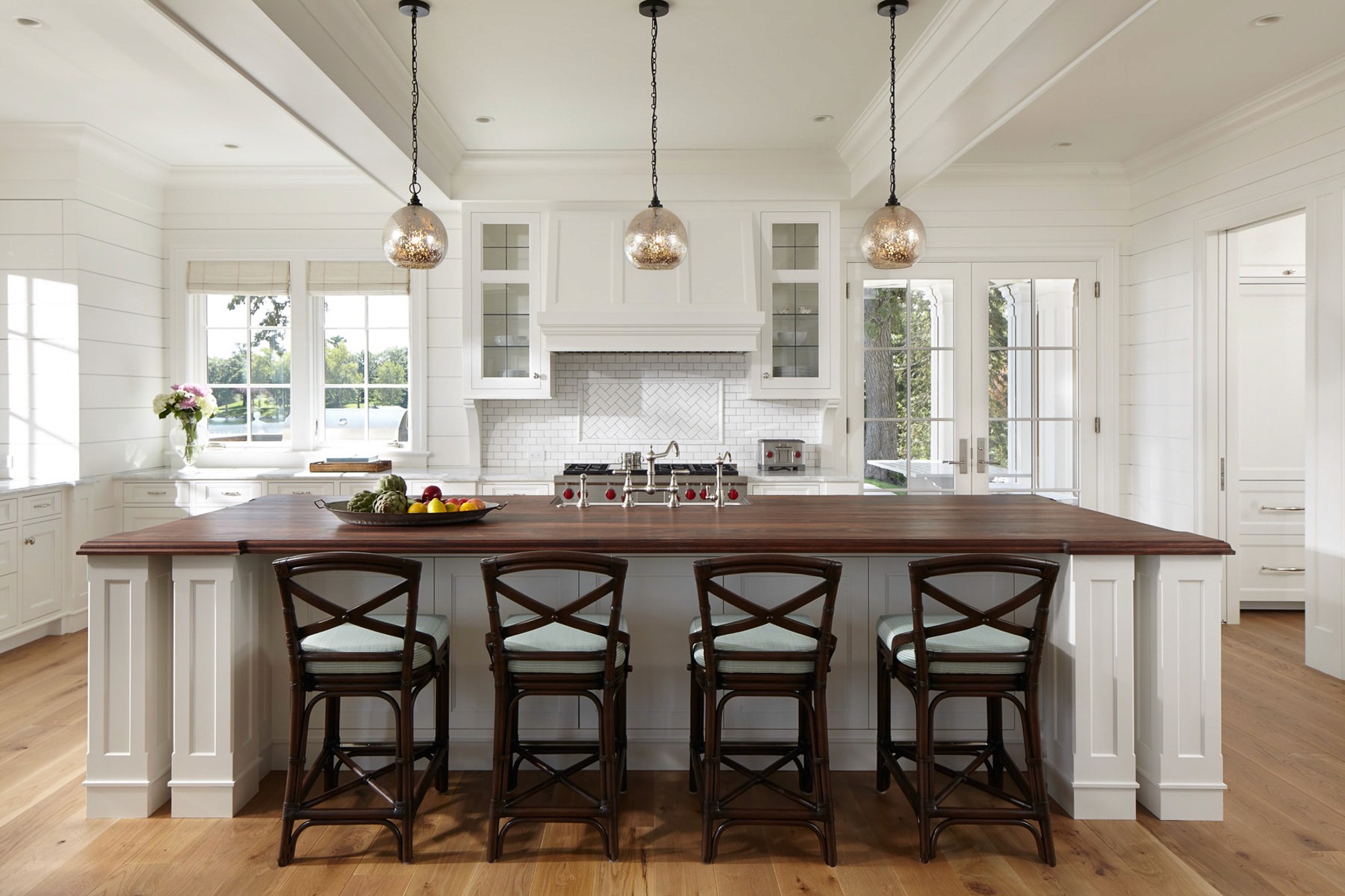A large, bright kitchen with white shiplap walls, a dark wood island counter, four bar stools, and glass pendant lights.