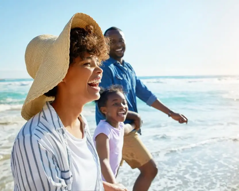 A happy family walks along the beach, smiling and enjoying a sunny day by the ocean. The image represents the freedom and peace of mind that come from using a cash-out refinance with Chris Lewis Home Loans to achieve financial goals and create lasting memories.