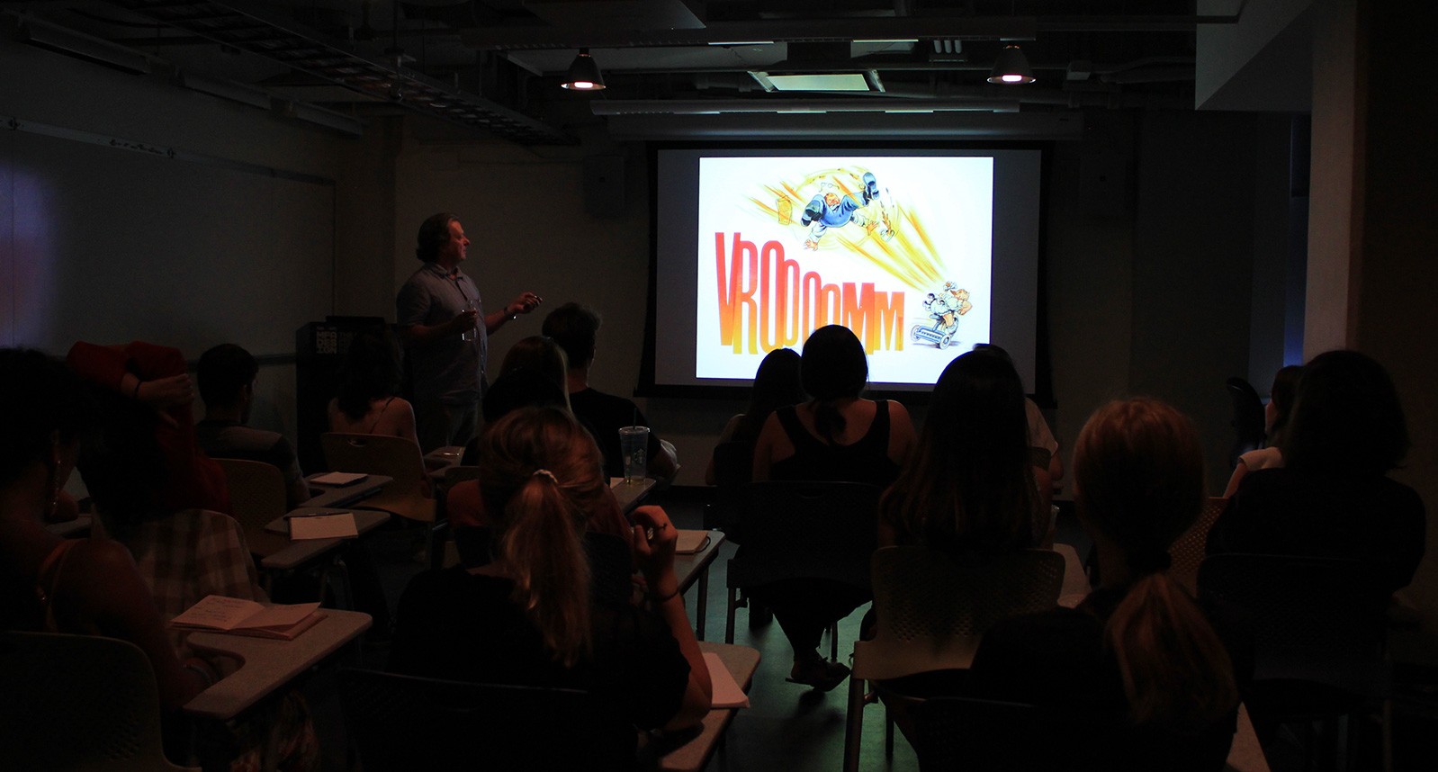 a man is presenting a comic book illustration projected on a wall to a room full of people