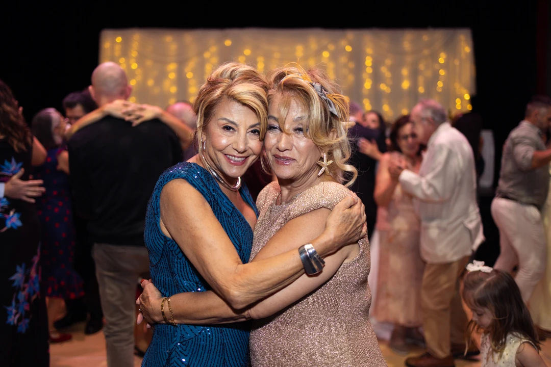 Sisters hugging at wedding in front of dancing guests
