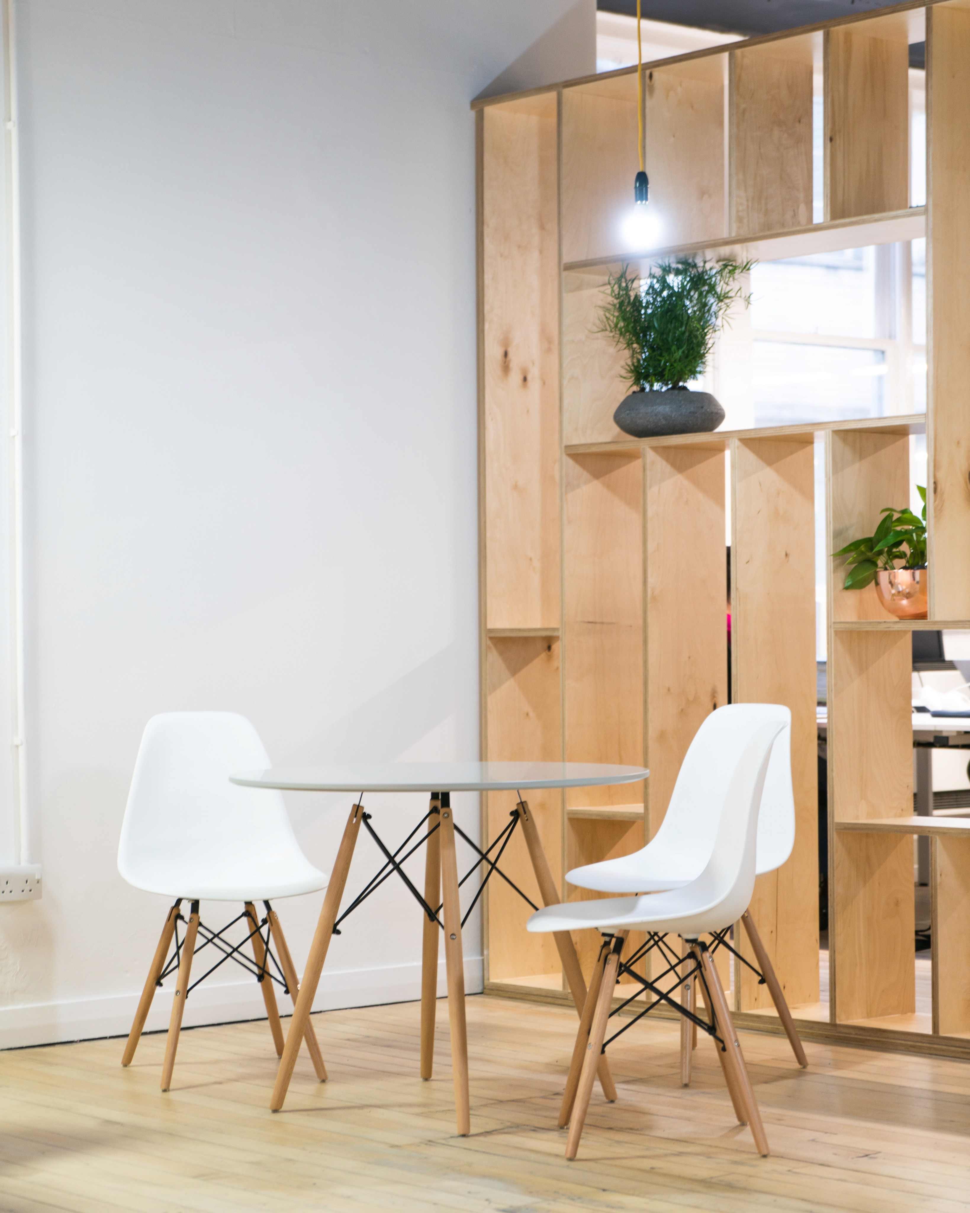 A photo of an office with stylish eames-style chairs surrounding a table, a plywood shelving unit behind them