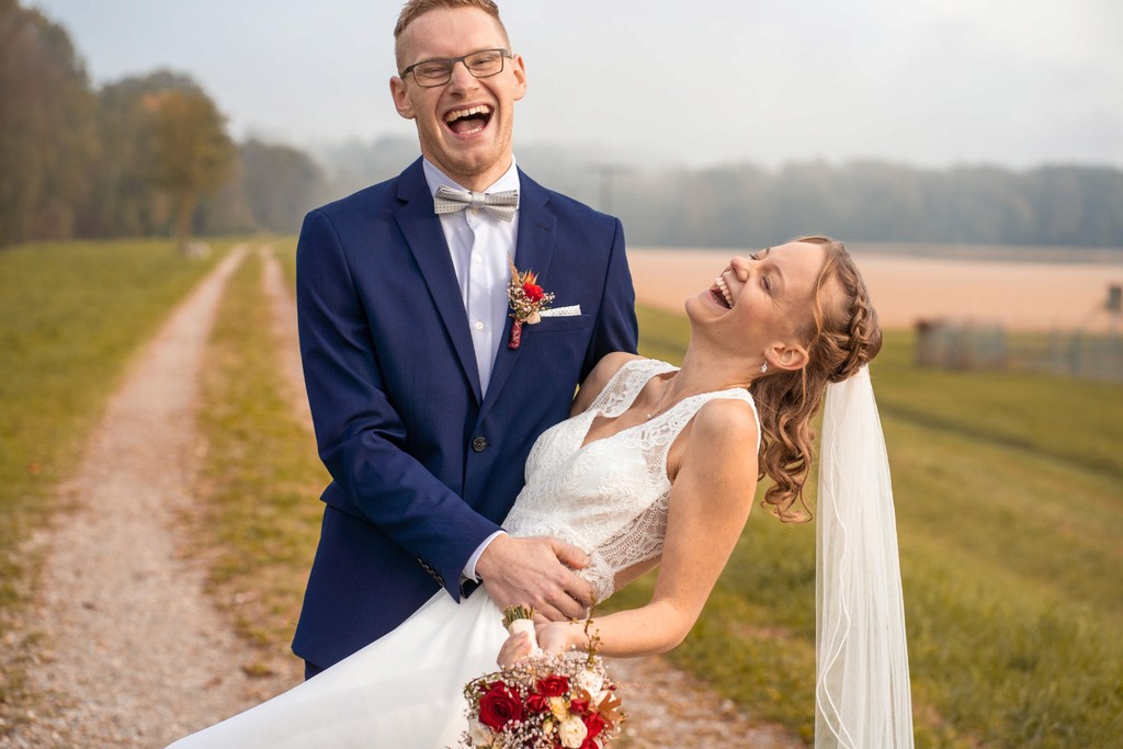 Brautpaar lacht und tanzt auf Feldweg während Hochzeitsshooting
