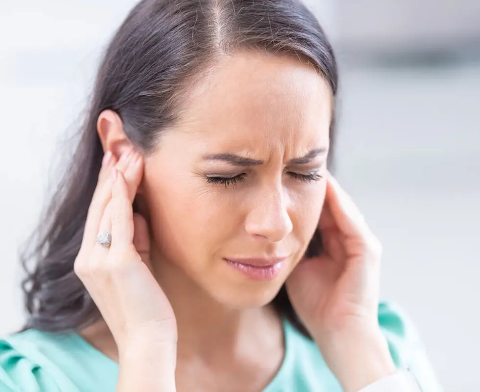 A woman is holding her head with a pained expression, indicating discomfort or a headache.