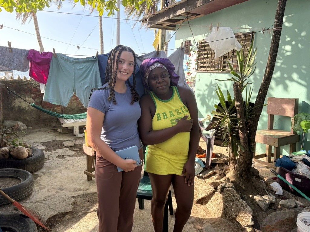 A girl with braided hair standing beside a woman outdoors.