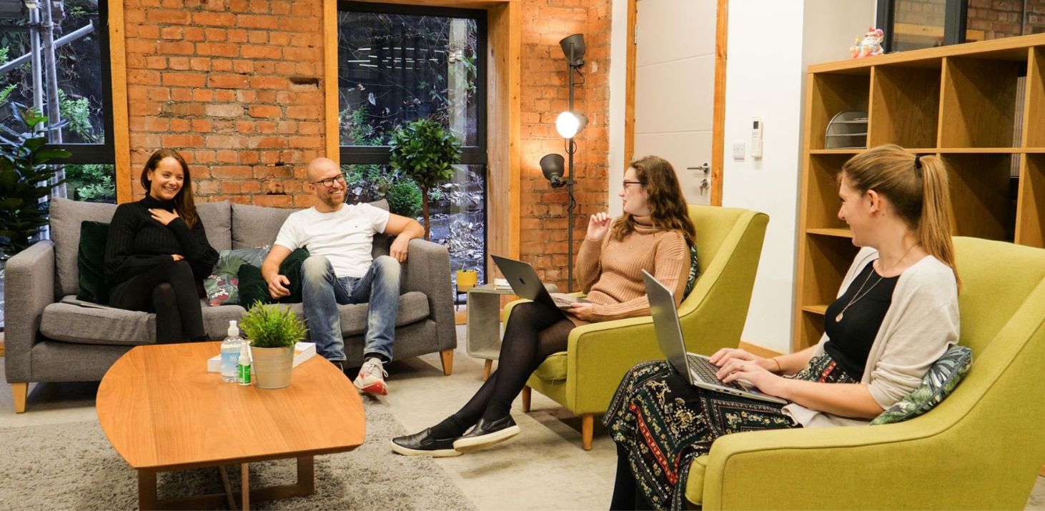 People talking in a warm room with chairs and an old-fashioned table.