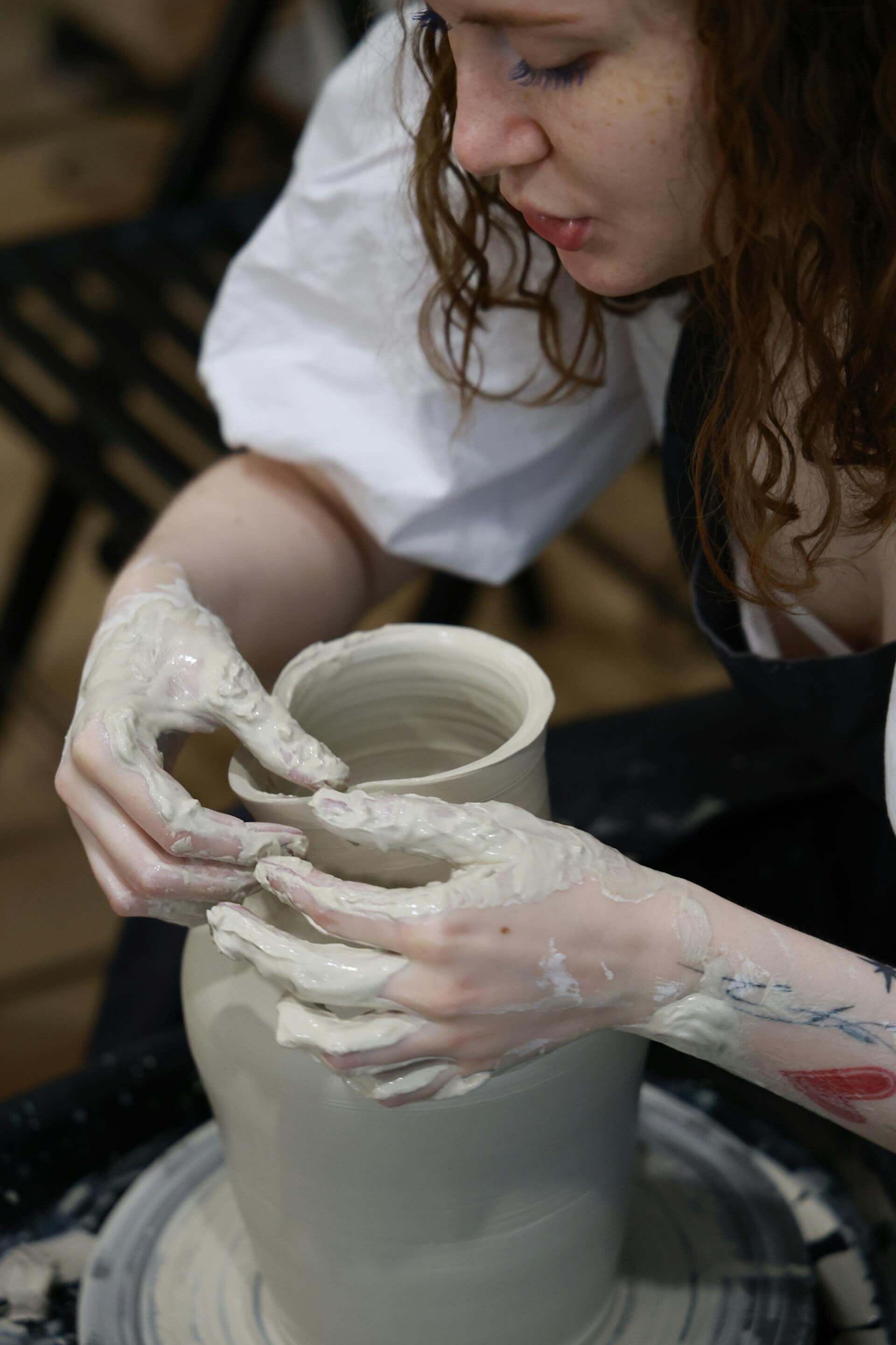 A woman skillfully shapes clay on a potter's wheel, creating a beautiful pot with focused concentration