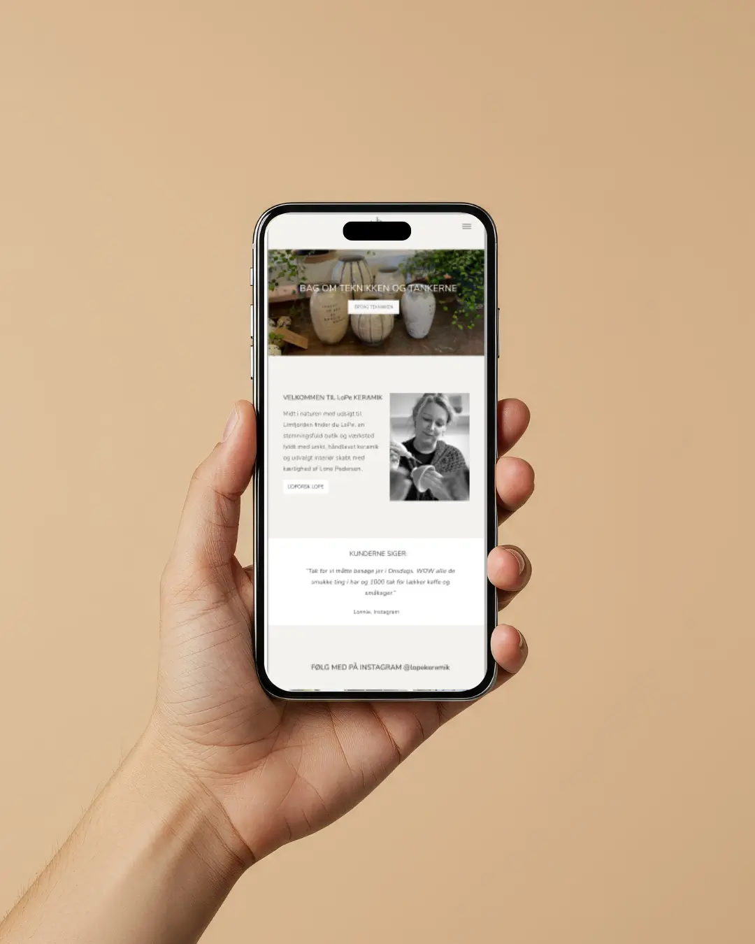 Hånd holdt telefon der viser keramik website, omgivet af en beige væg