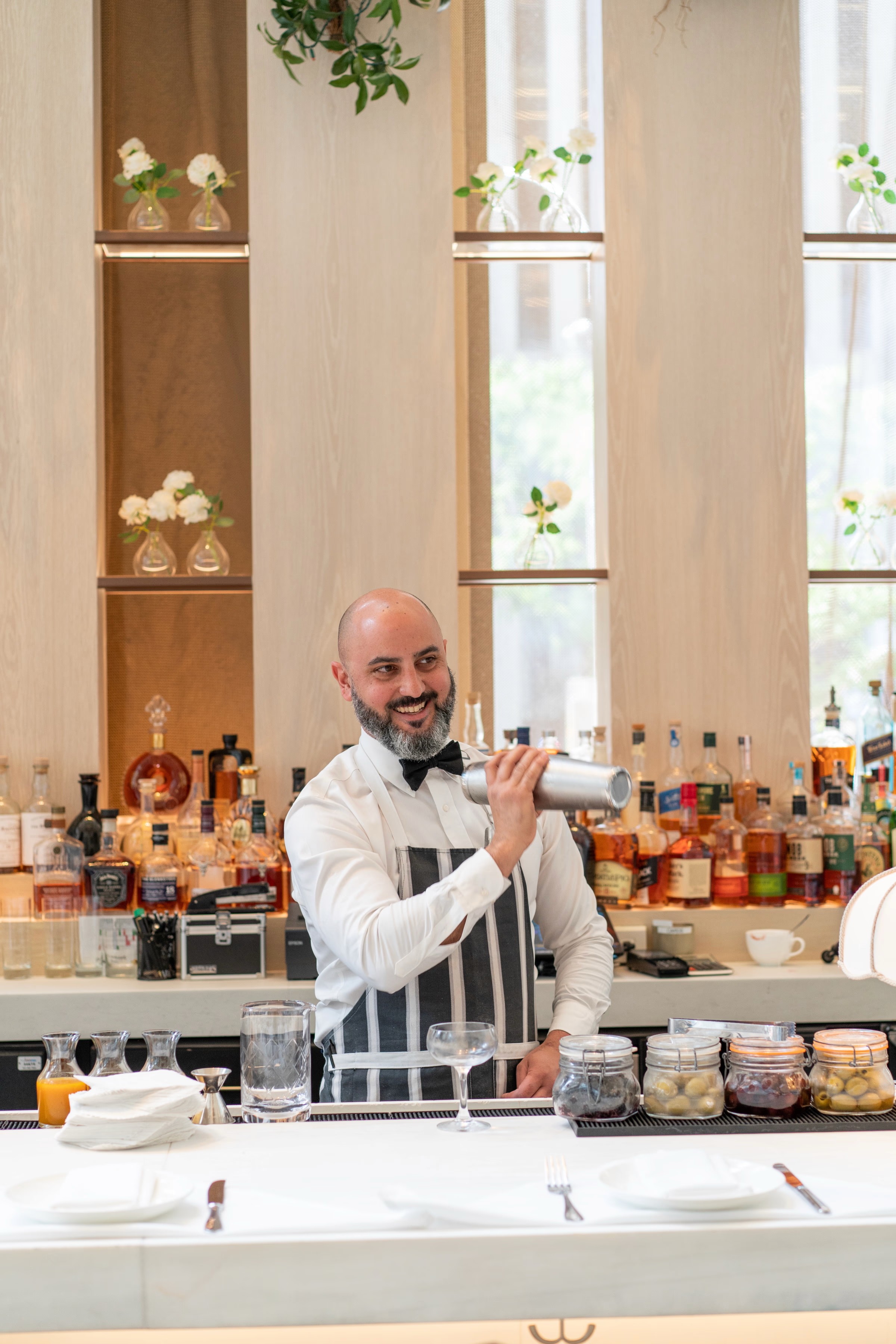 A man sits at a table in a bright room, speaking to an audience while holding a microphone.