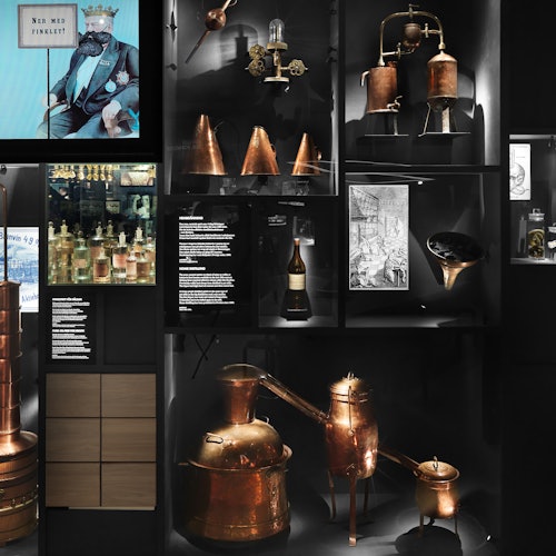 Vintage lepárló berendezések, réz aparátusok, történelmi fényképek és különféle műtárgyak bemutatása múzeumi környezetben.