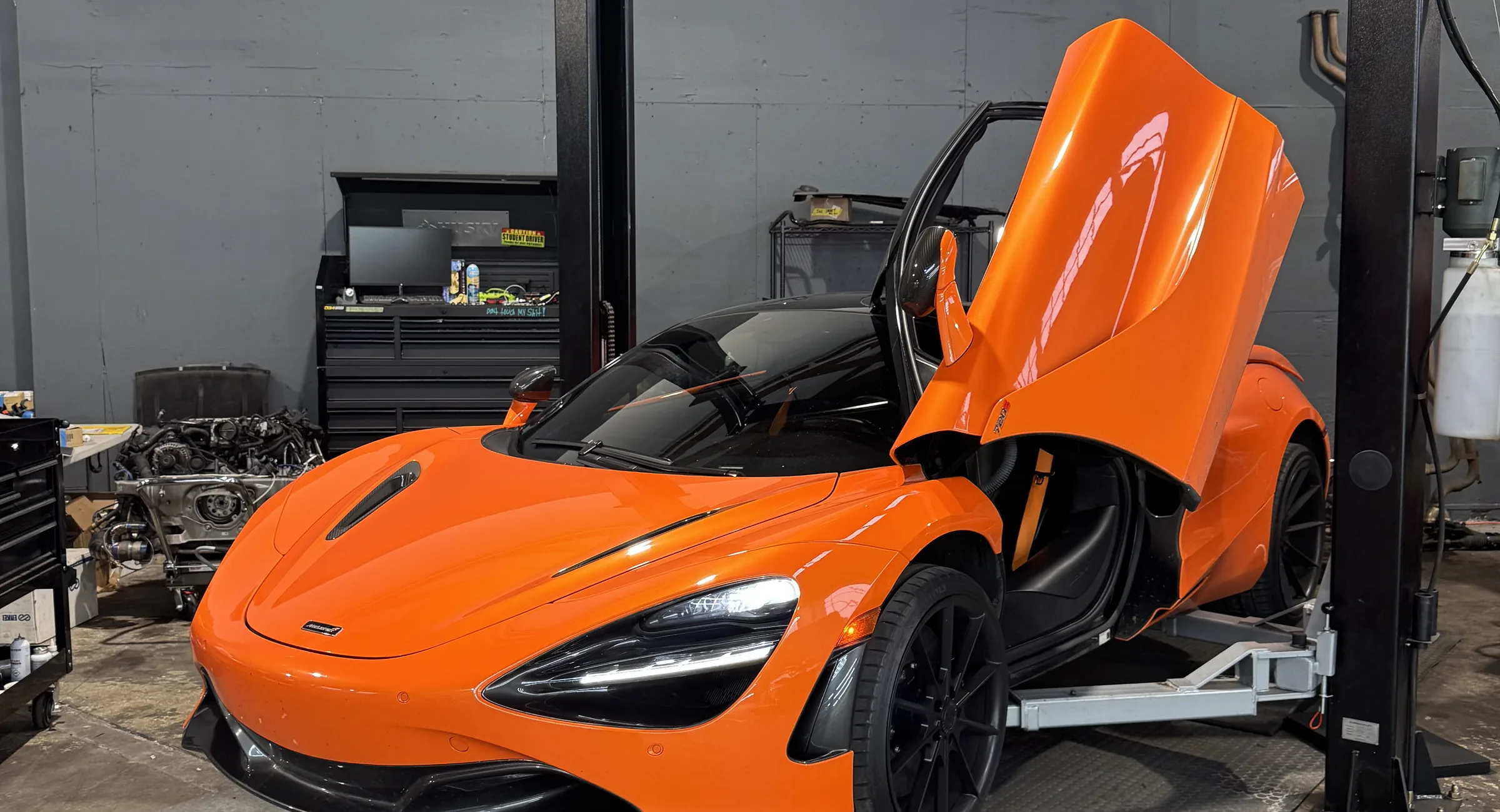 Orange McLaren 720S with its doors up beside a lift in the 714 Technik service bay
