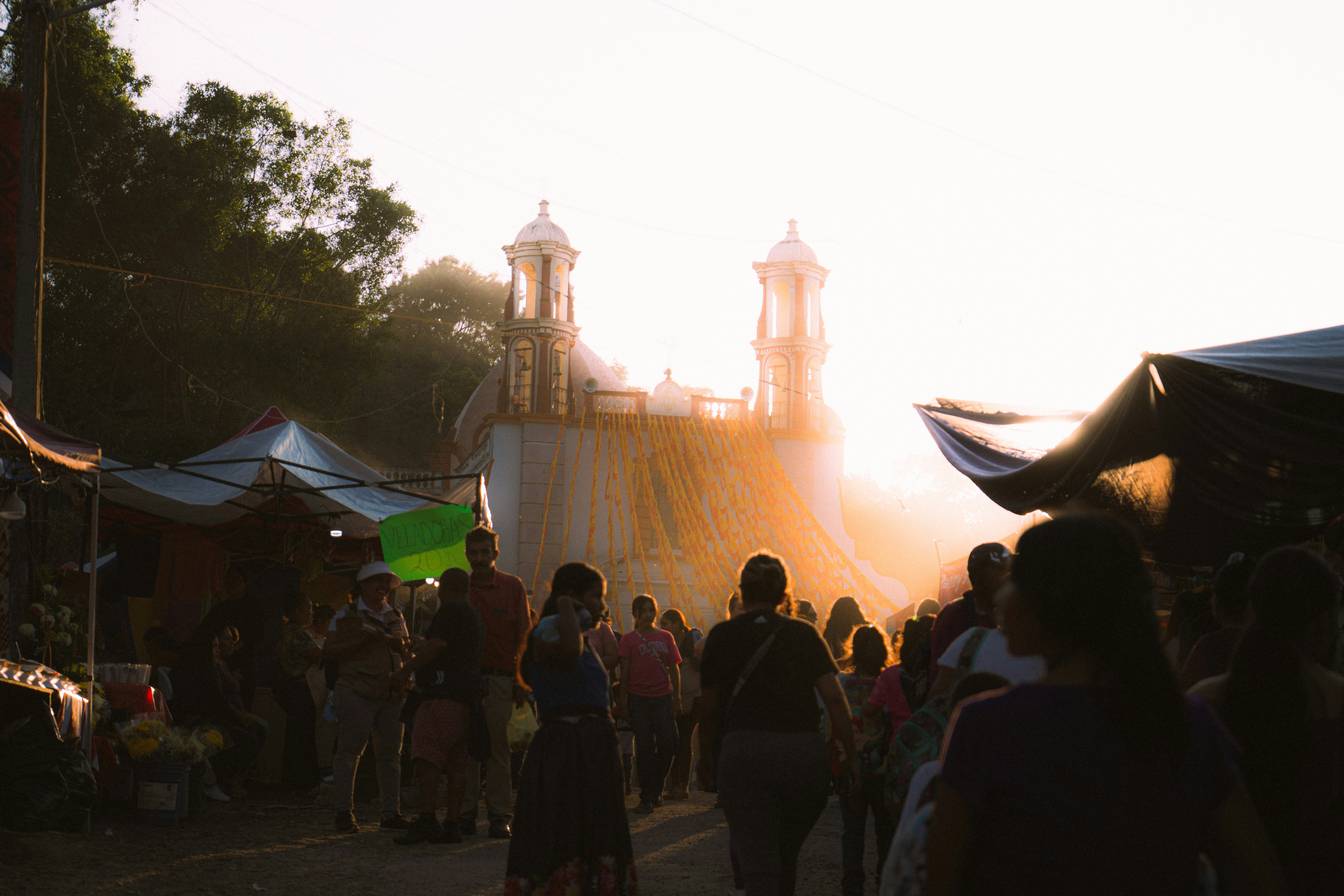 People walk past market stalls towards a church at sunset