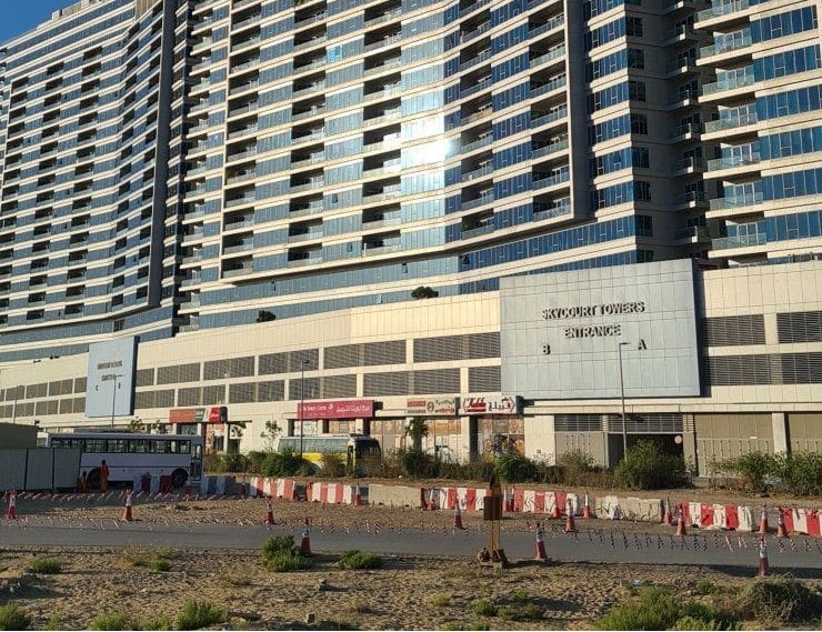 Entrance view of Skycourt Towers Dubai showing retail spaces and residential balconies for real estate listings.