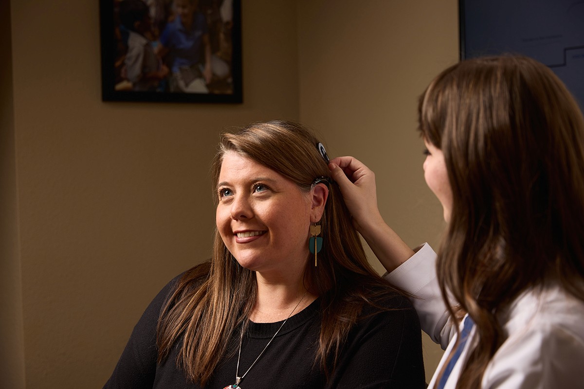 Two women are smiling, one is styling the hair of the other in a cozy indoor setting.