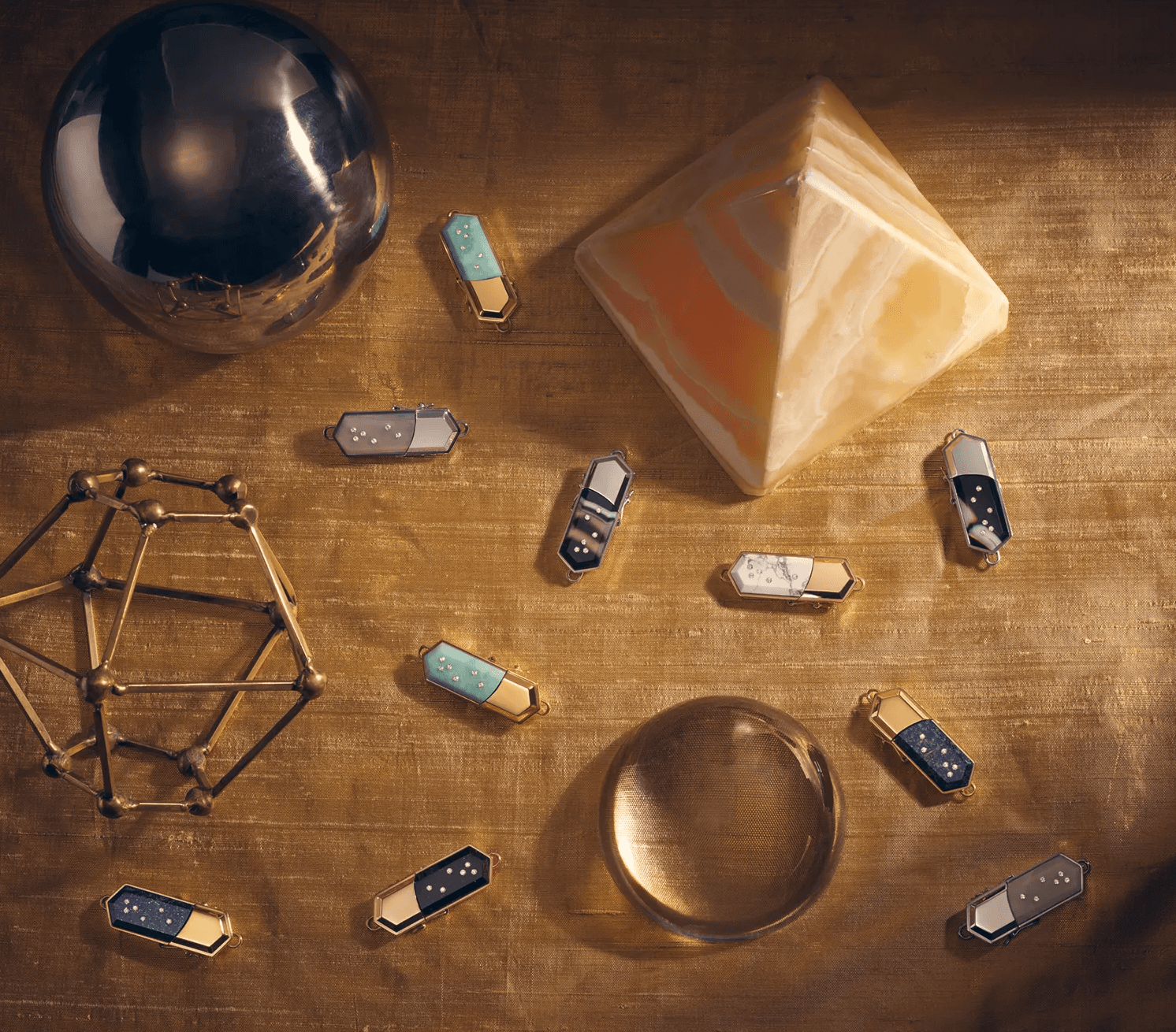 Talsam smart jewelry charms arranged with sculptural objects on a warm metallic surface