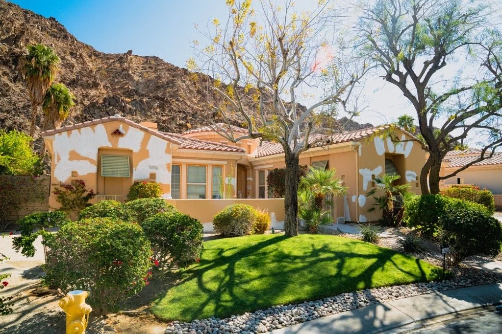 Modern two-story home with large glass windows, warmly lit interiors, and a balcony. Surrounded by trees and a manicured lawn at dusk. Cozy ambiance.