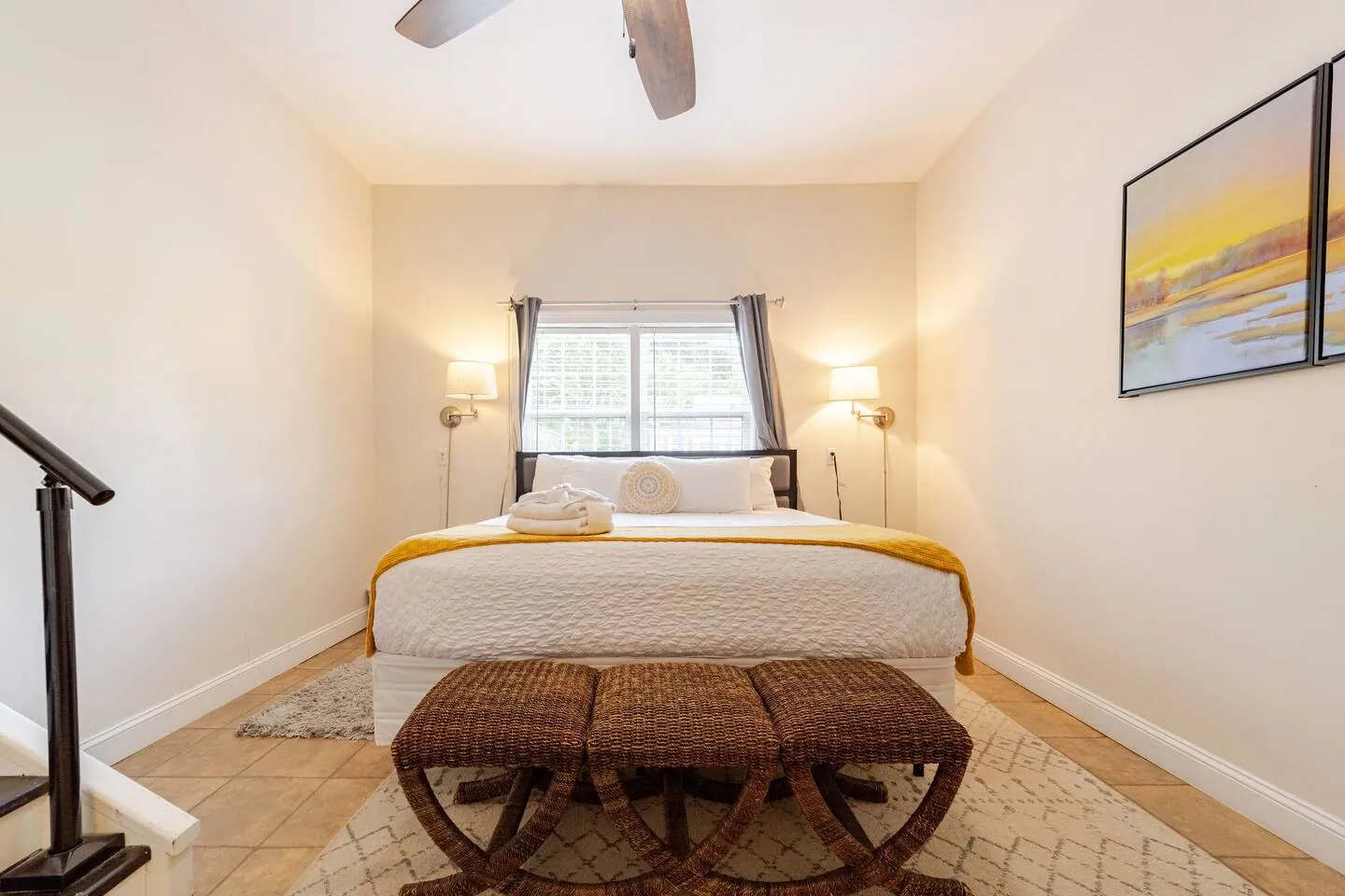 The stepped-down suite: king bed with a yellow throw and a rattan bench, three steps from the kitchen