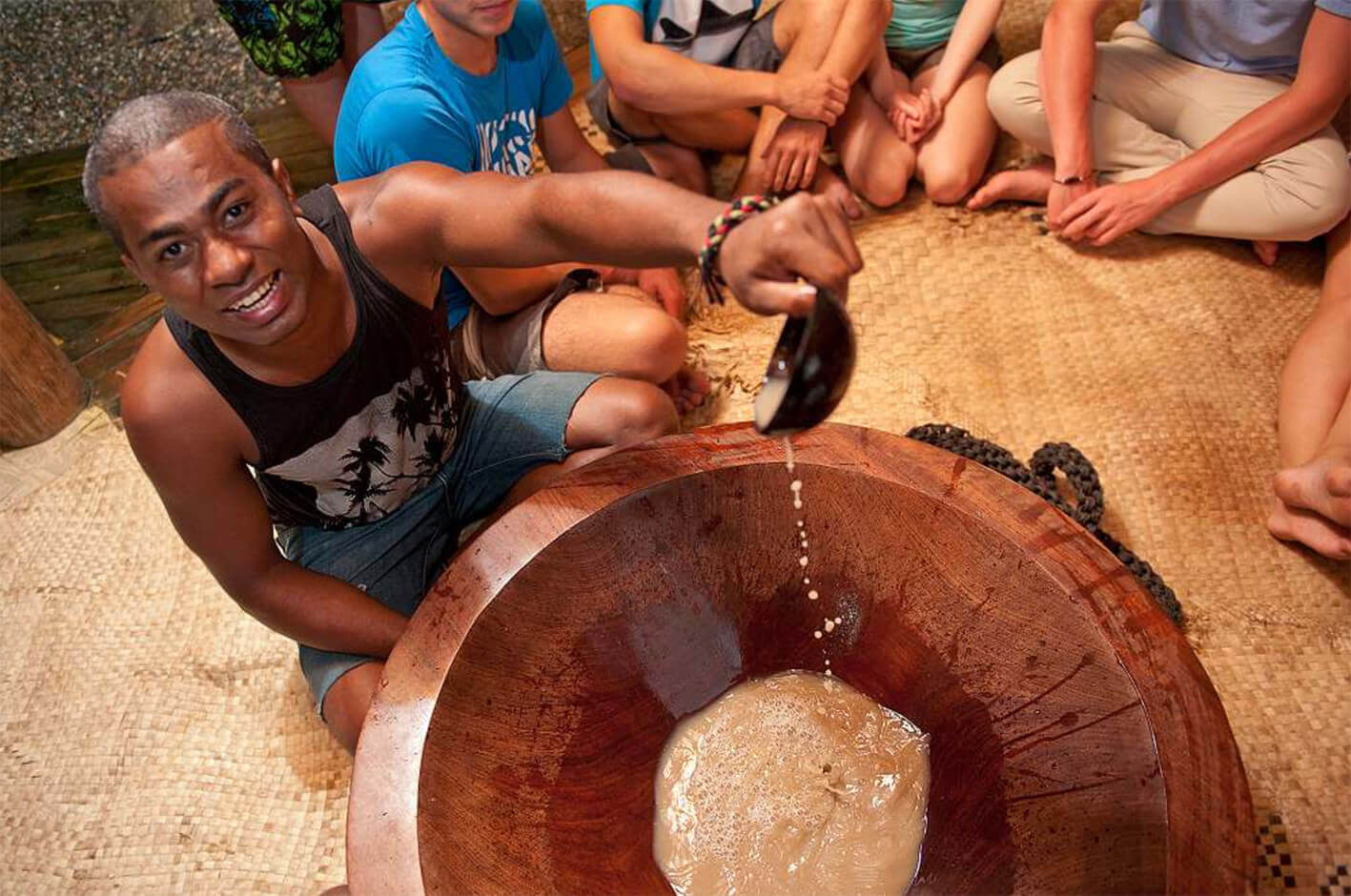 Fijian man smiles, pouring Kava into a tanoa during an authentic Fijian hospitality ceremony.