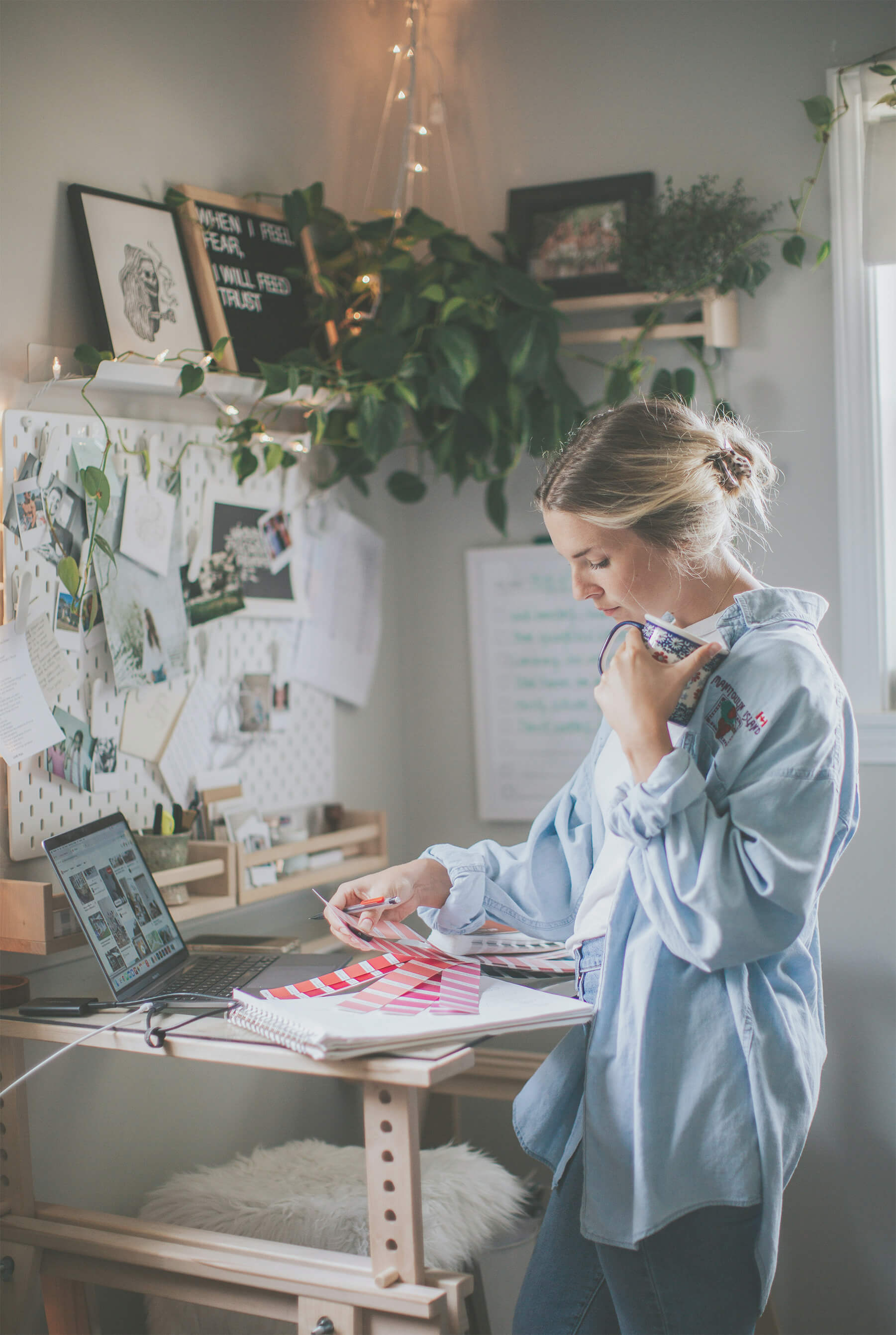 Designer reviewing color swatches and materials at standing desk with mood board and plants.