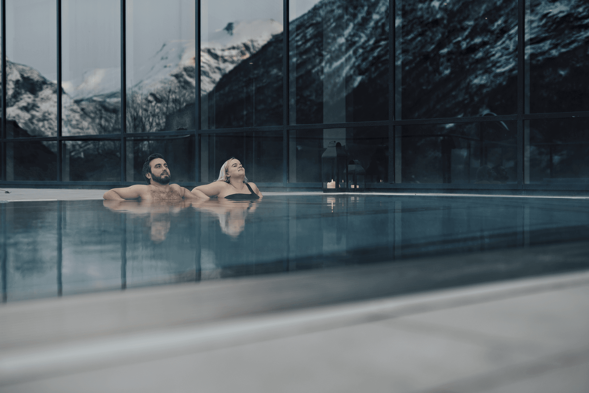 A serene indoor pool scene with modern architecture, reflecting mountains and natural light.