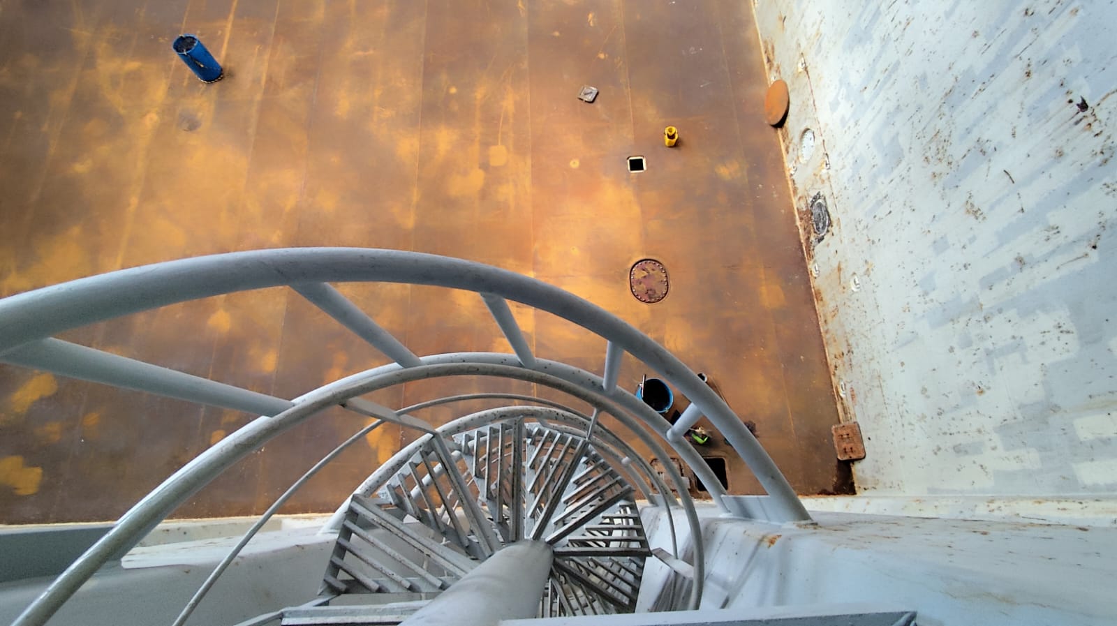 Spiral access ladder inside cargo hold, looking down to tank top after cleaning following coal cargo operations.