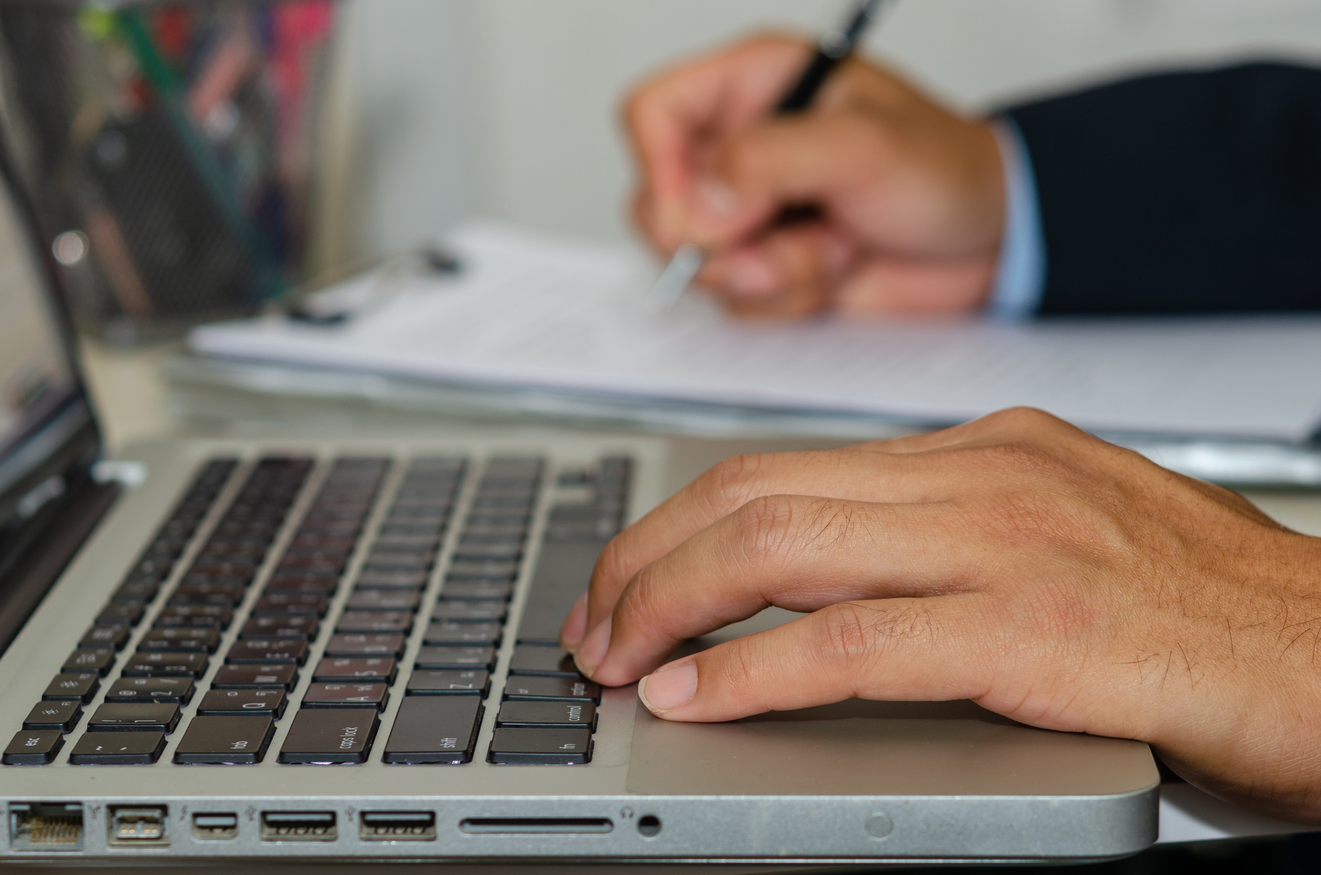 Image of a close-up of hands typing on a laptop beside legal documents.