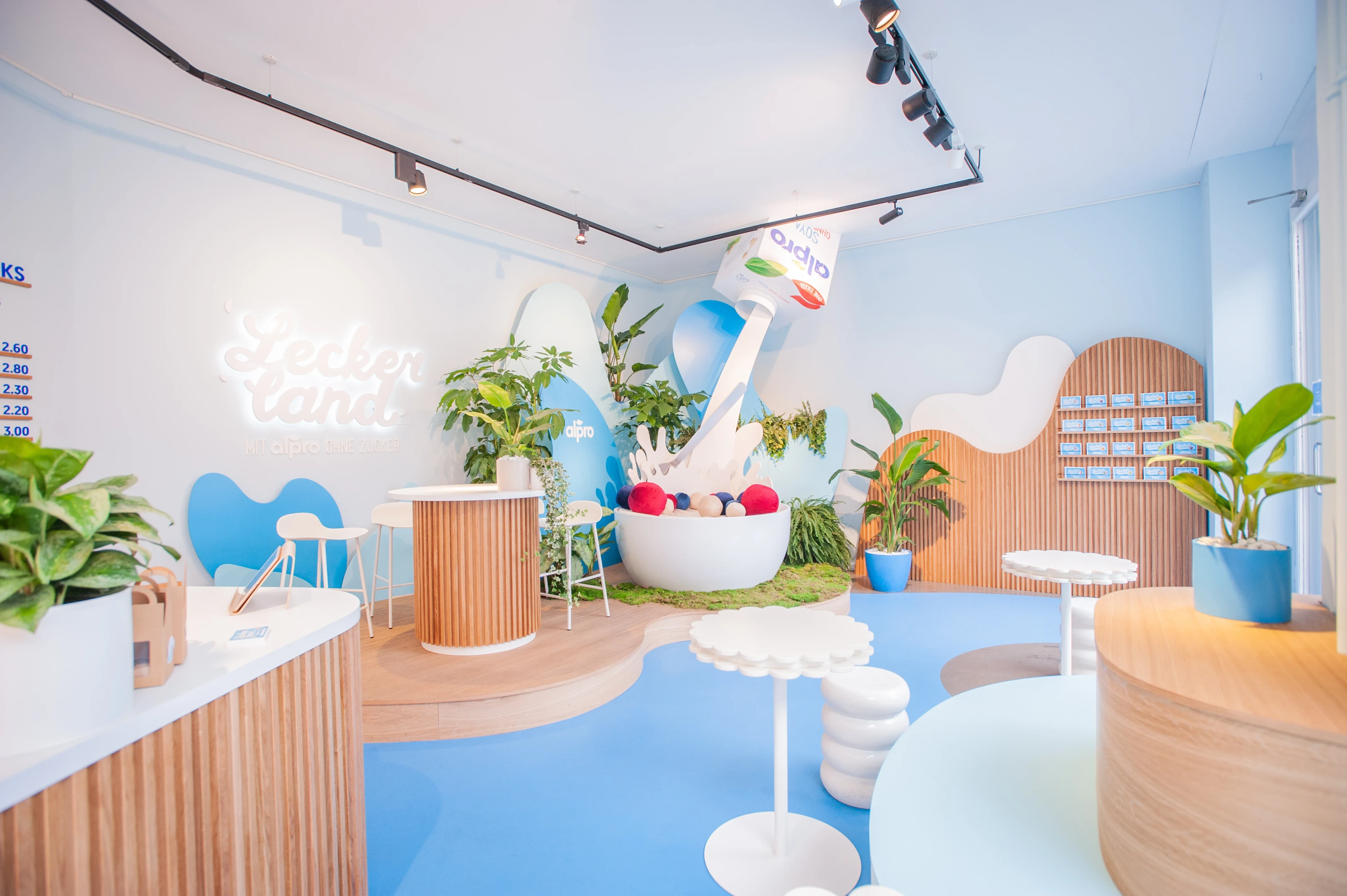 Interior of the Alpro Leckerland pop-up with giant cereal-bowl installation, wood-slat arches and playful white furniture.