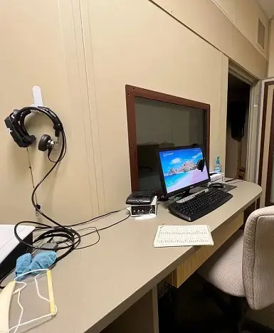 A desk setup featuring a monitor, headphones, and a notepad in a simple room.
