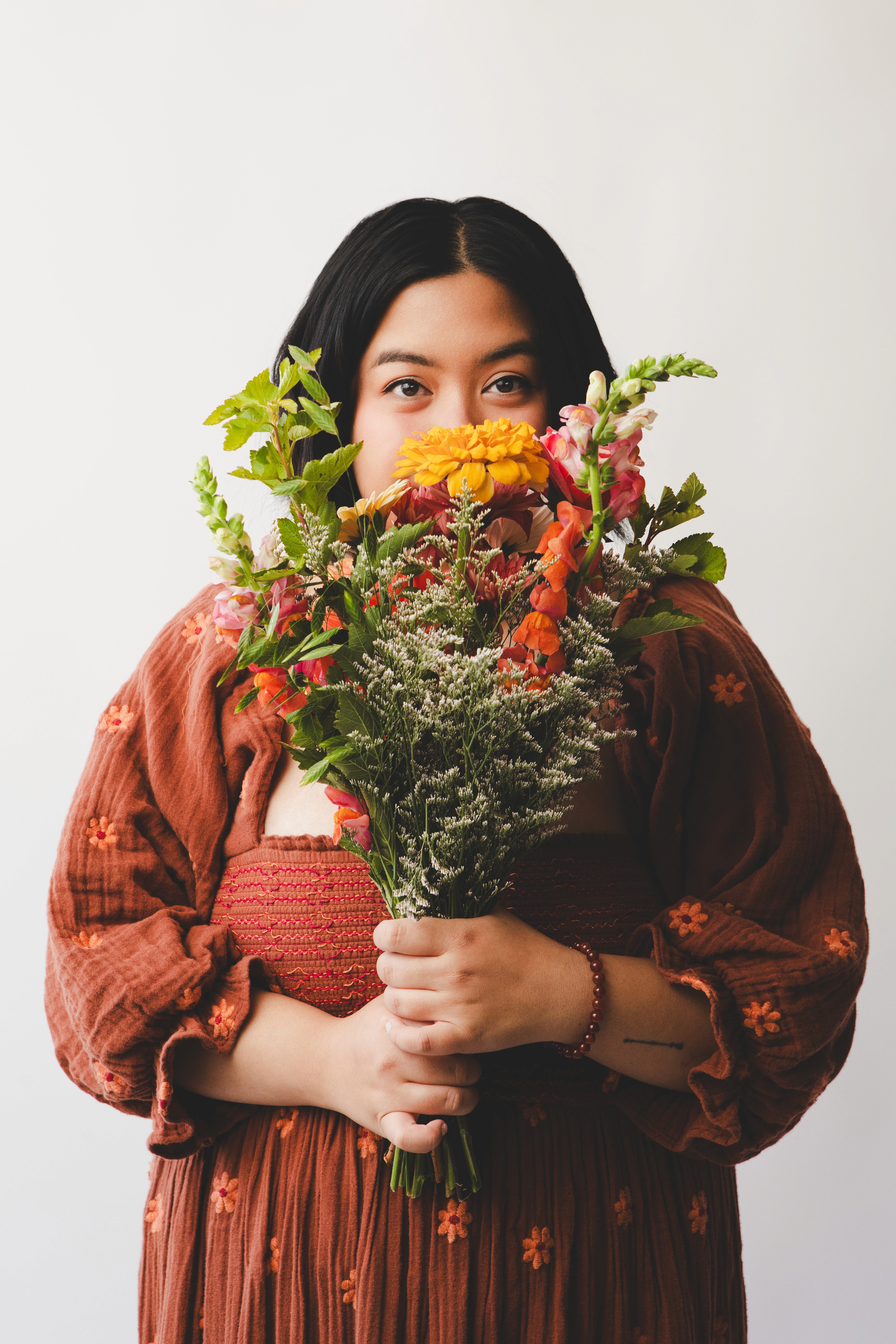 photo of the designer wearing orange dress and holding flowers against white backdrop